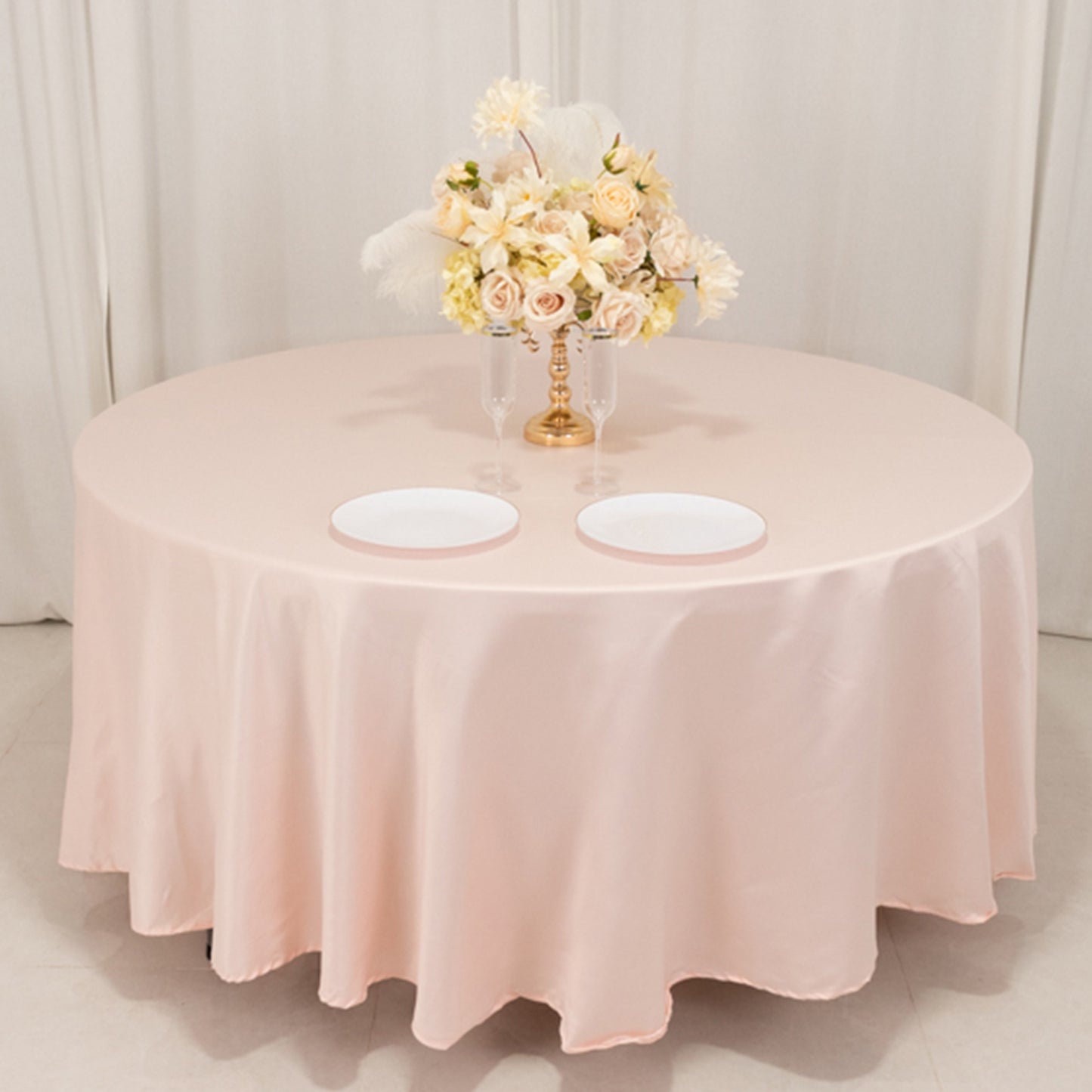 Blush satin round tablecloth draped over a round table with floral centerpiece.