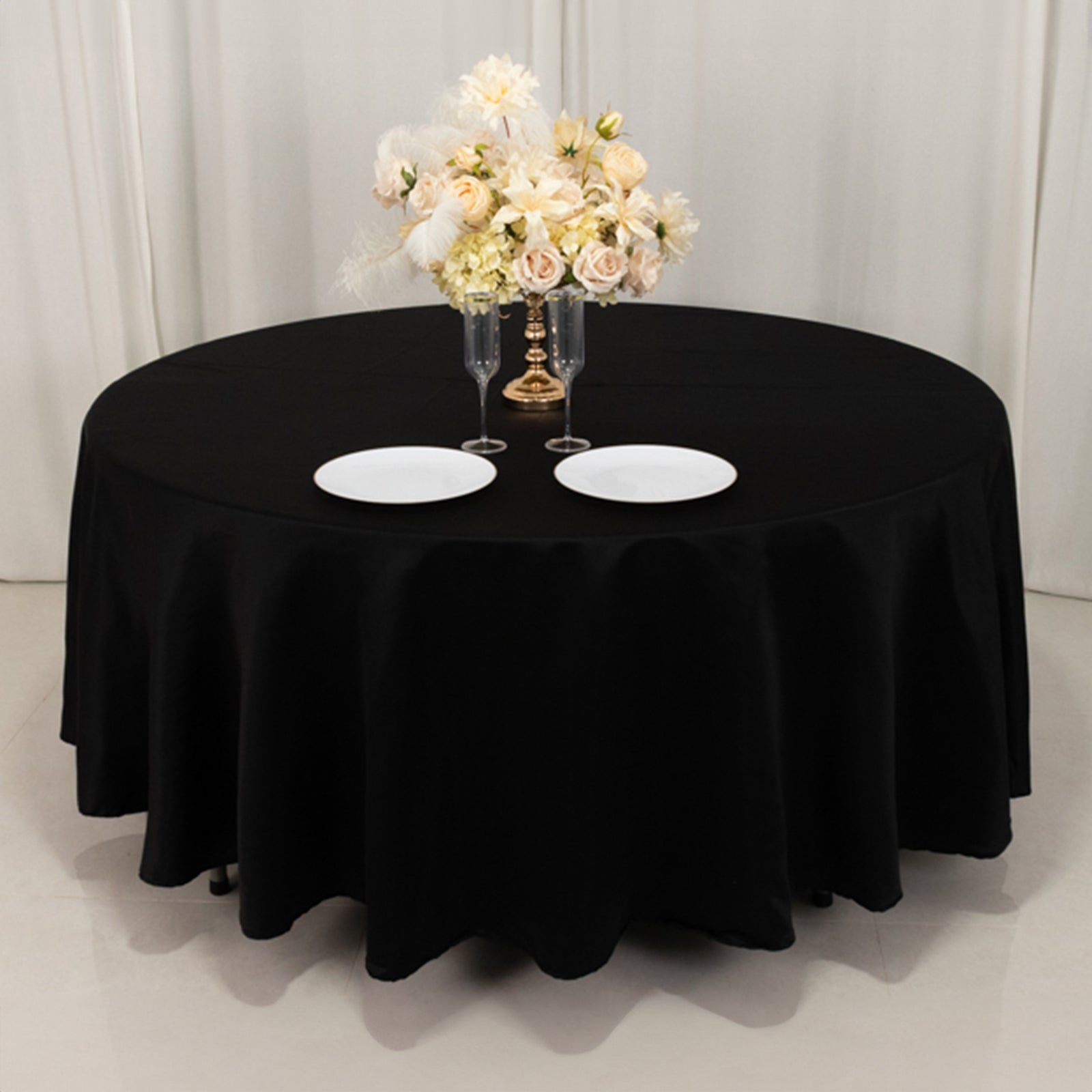 Black round tablecloth with floral centerpiece and white plates.