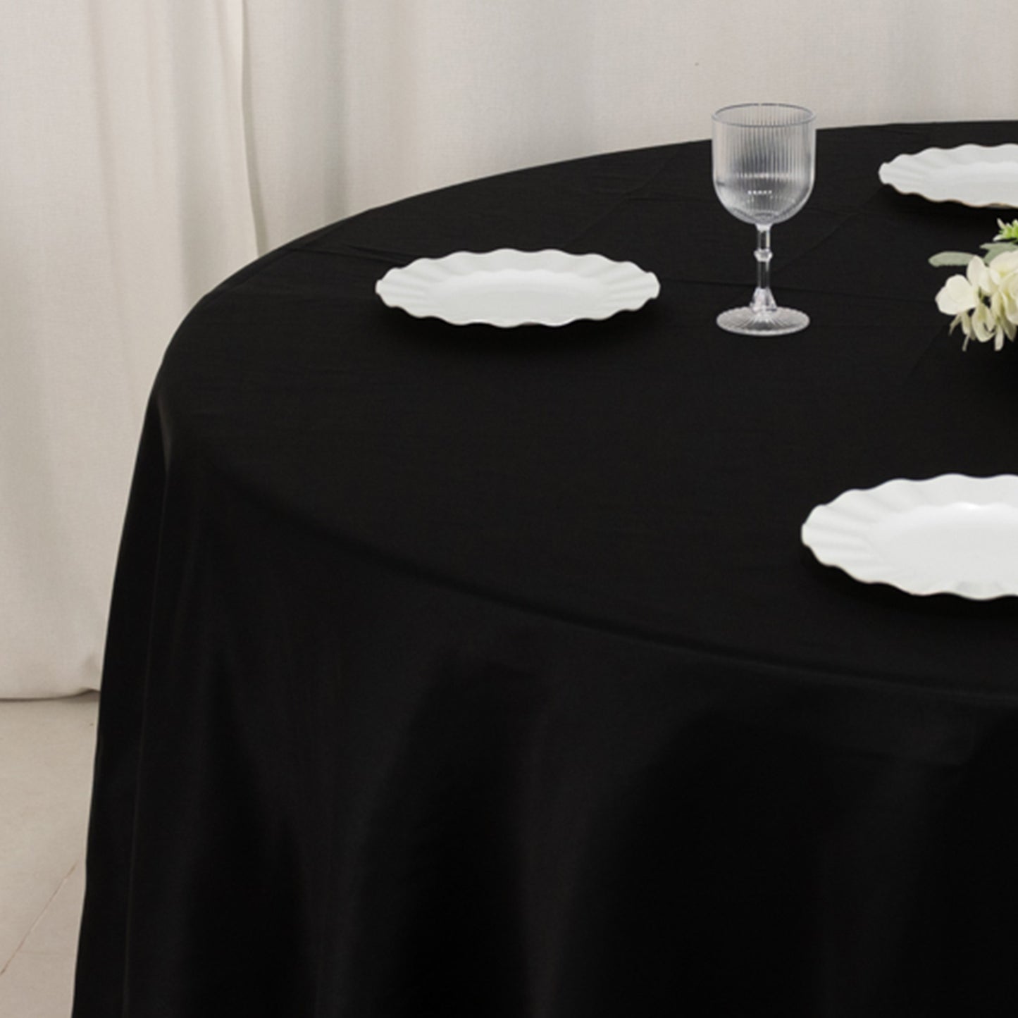 Black round tablecloth on a dining table with white plates and a glass.