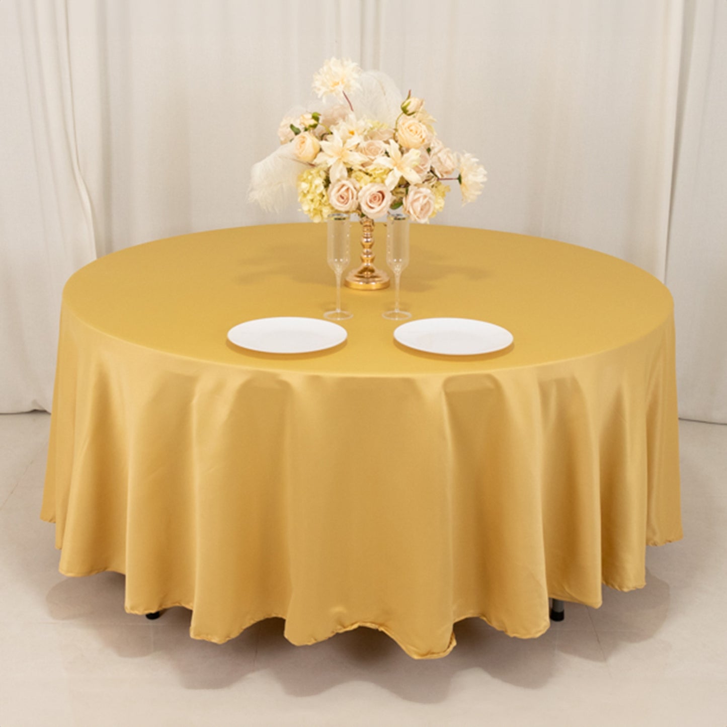 Champagne round satin tablecloth with floral centerpiece and plates.