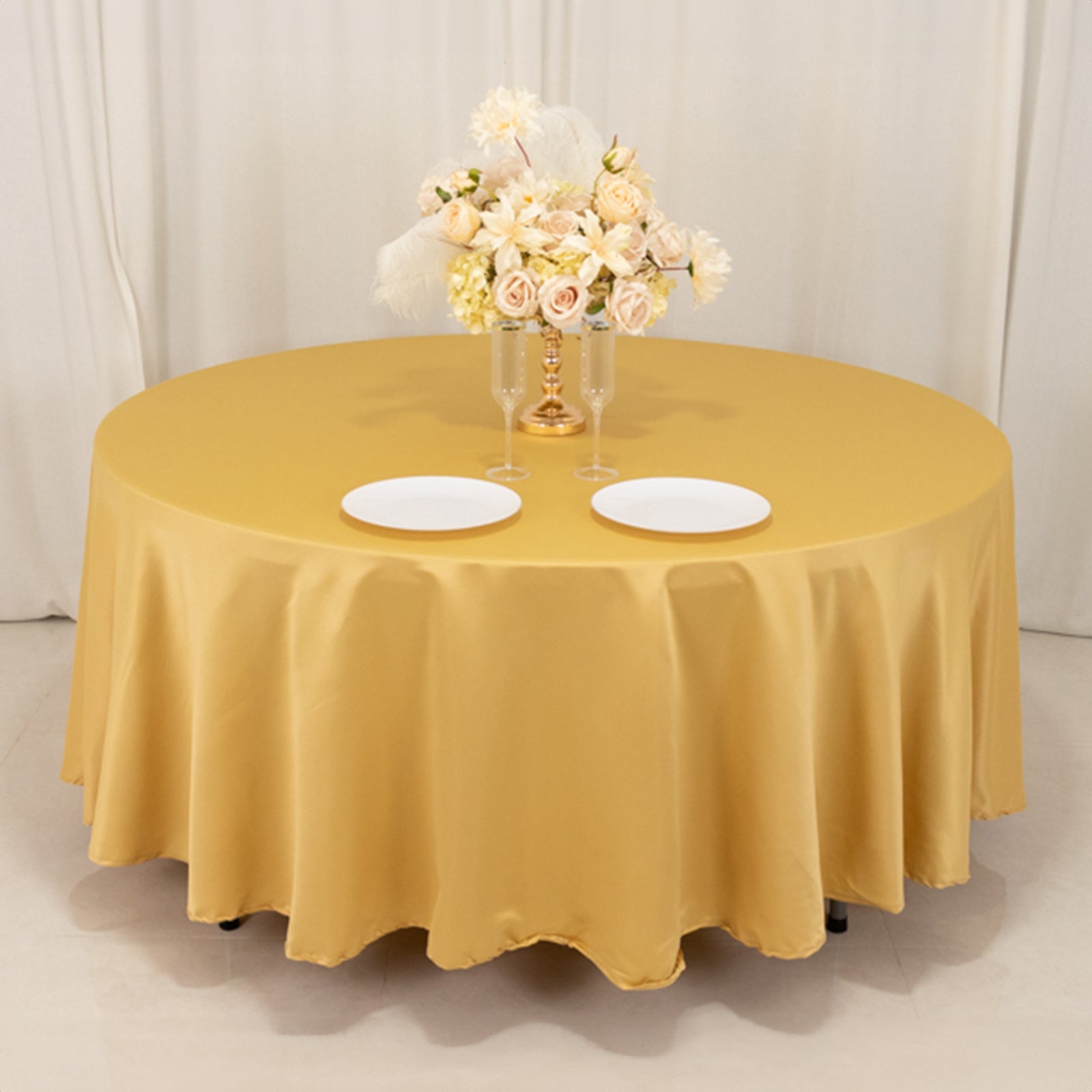 Champagne round satin tablecloth with floral centerpiece and plates.