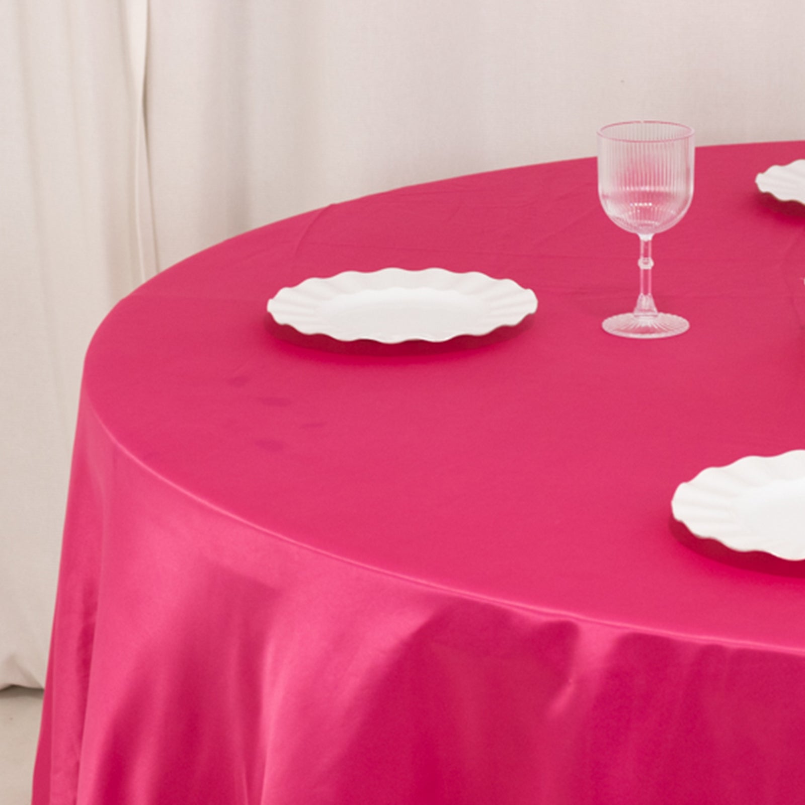 Fuchsia round satin tablecloth with white plates on a table.