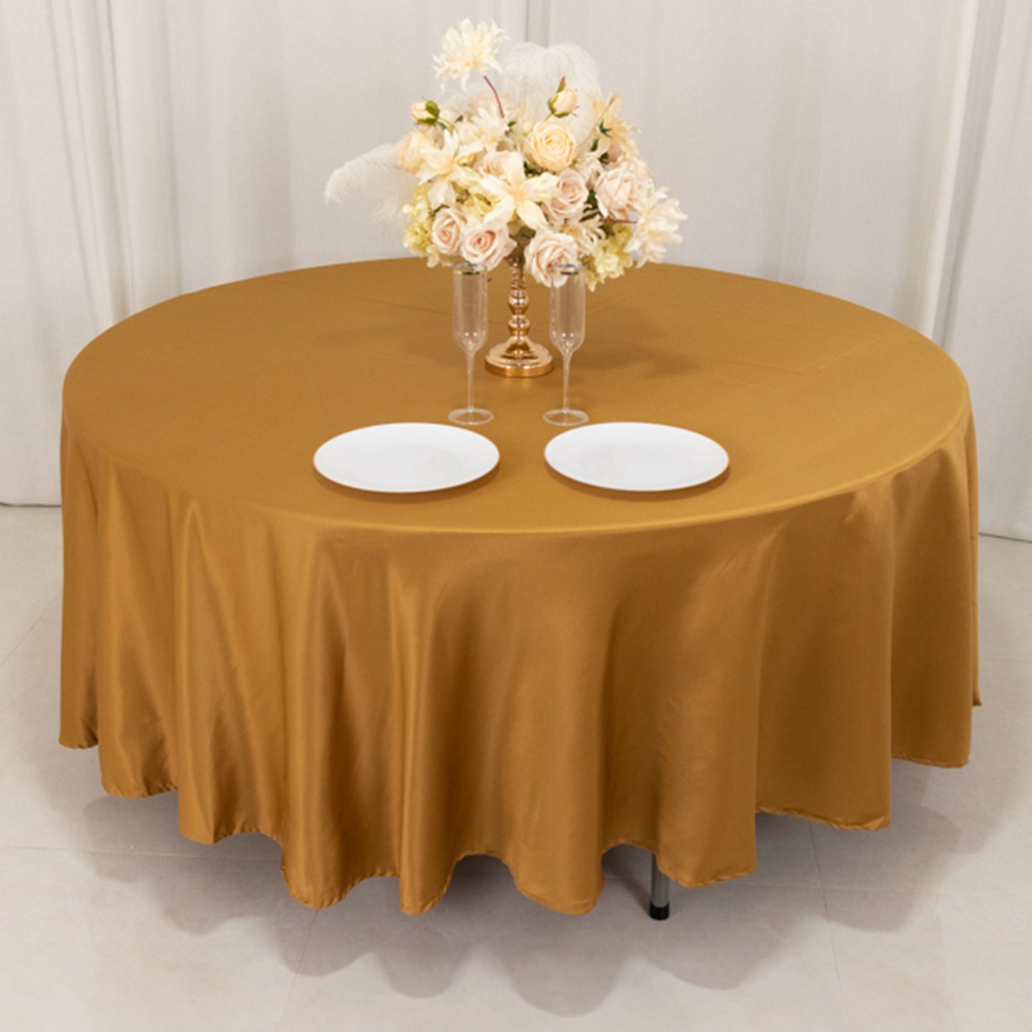 Gold round tablecloth with elegant floral centerpiece and dinner plates.