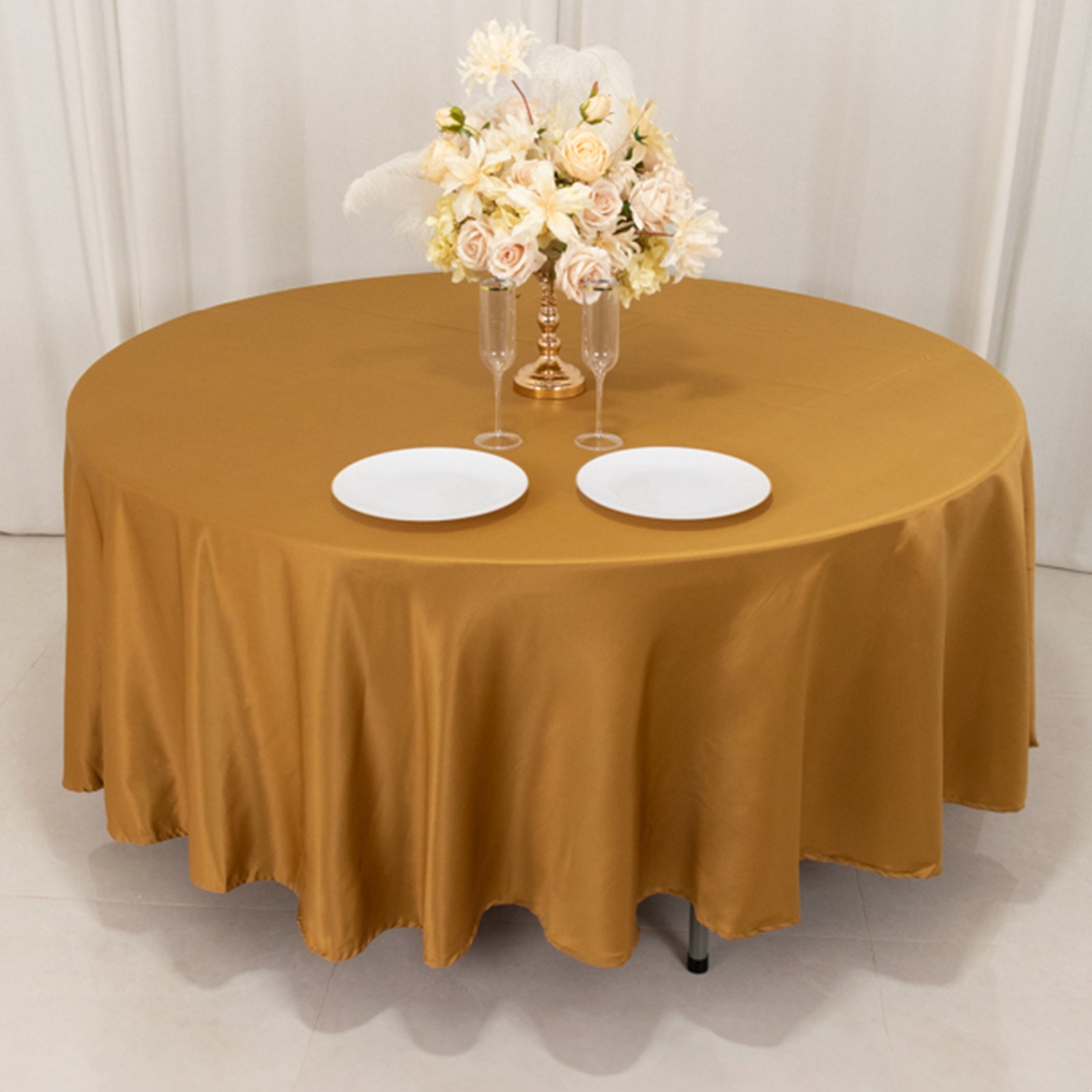 Gold round tablecloth with elegant floral centerpiece and dinner plates.