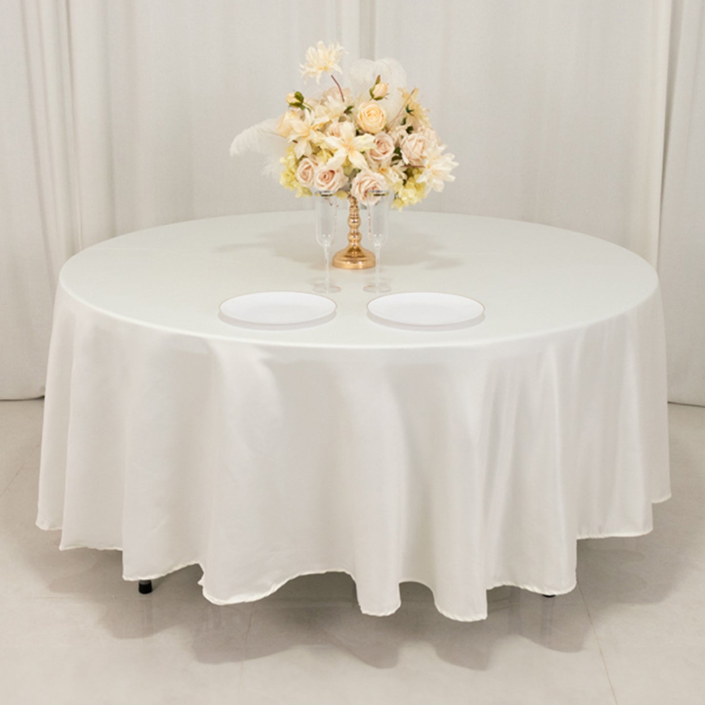 Ivory round satin tablecloth with a floral centerpiece and two plates.