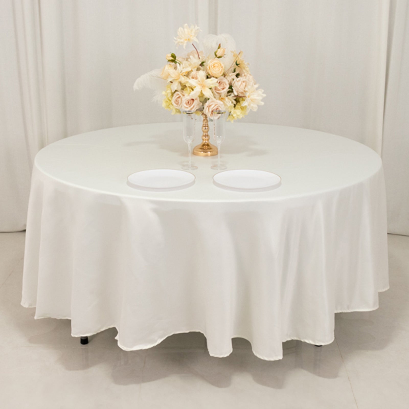 Ivory round satin tablecloth with a floral centerpiece and two plates.