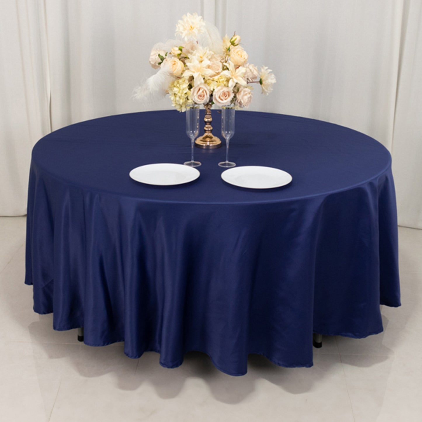 Navy blue satin round tablecloth with floral centerpiece and white plates.