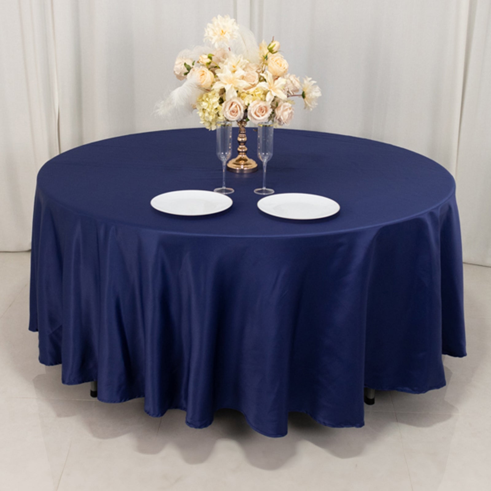 Navy blue satin round tablecloth with floral centerpiece and white plates.