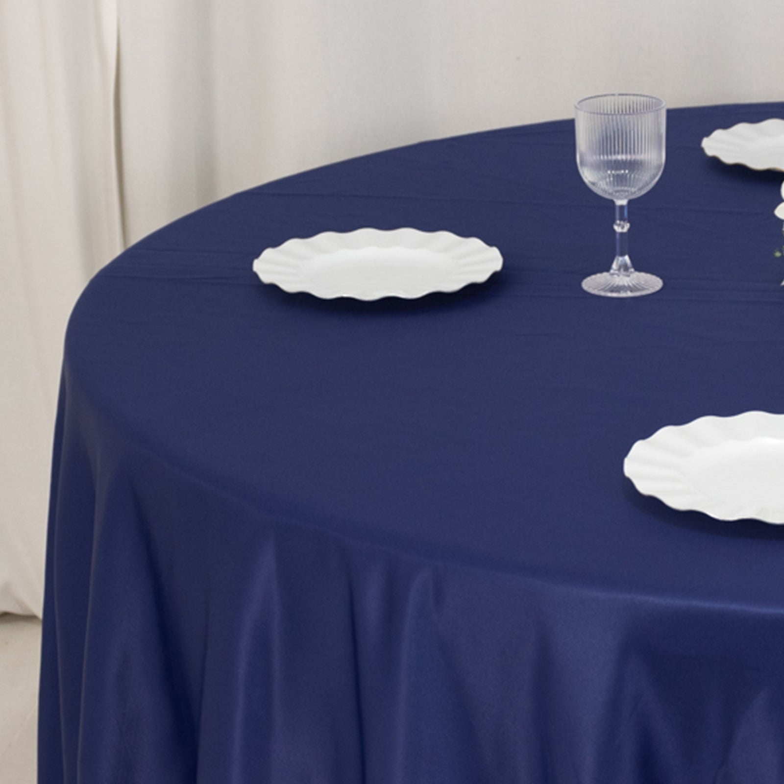 Navy blue satin round tablecloth with white plates and glass on a table.