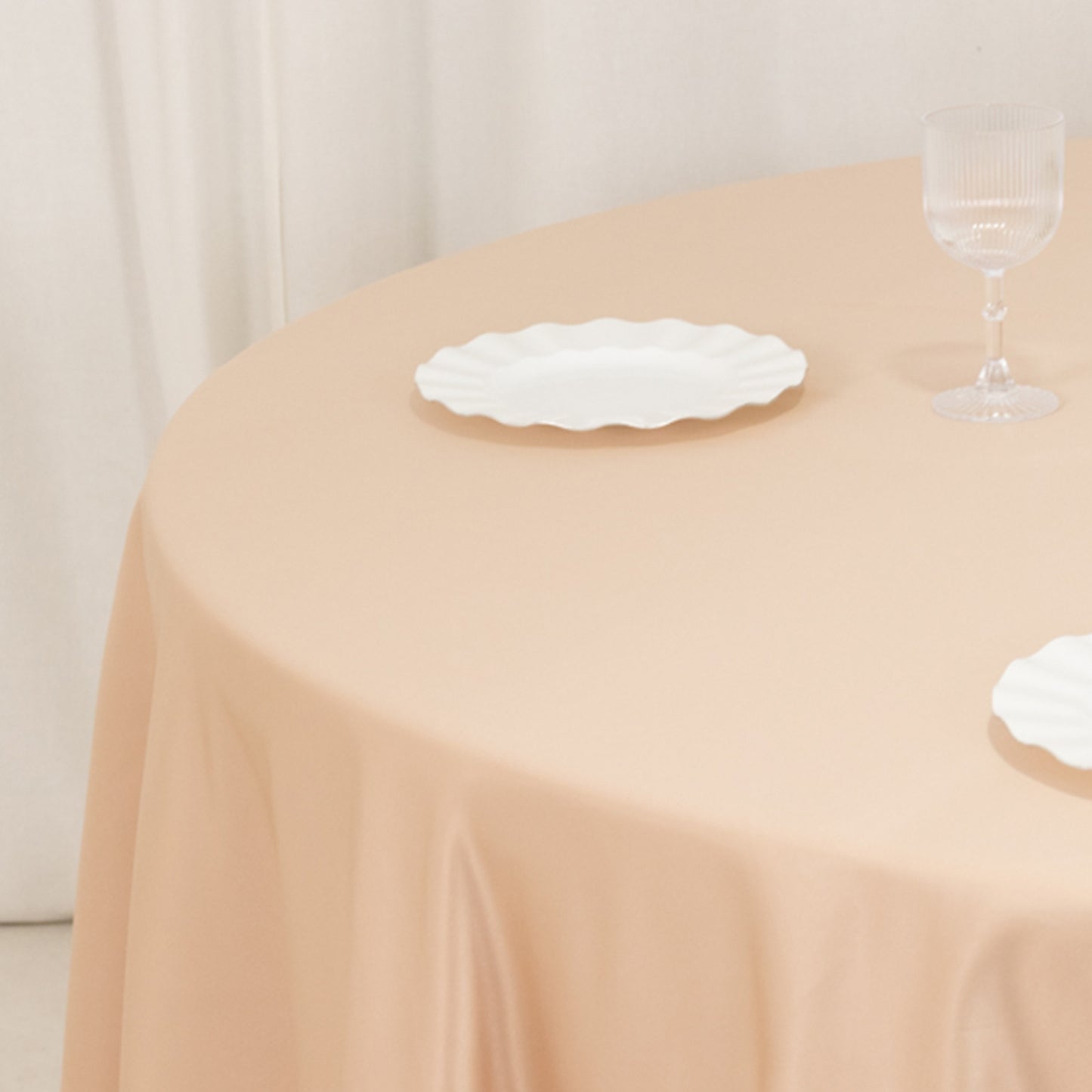 Nude satin round tablecloth on a table with plates and glassware.