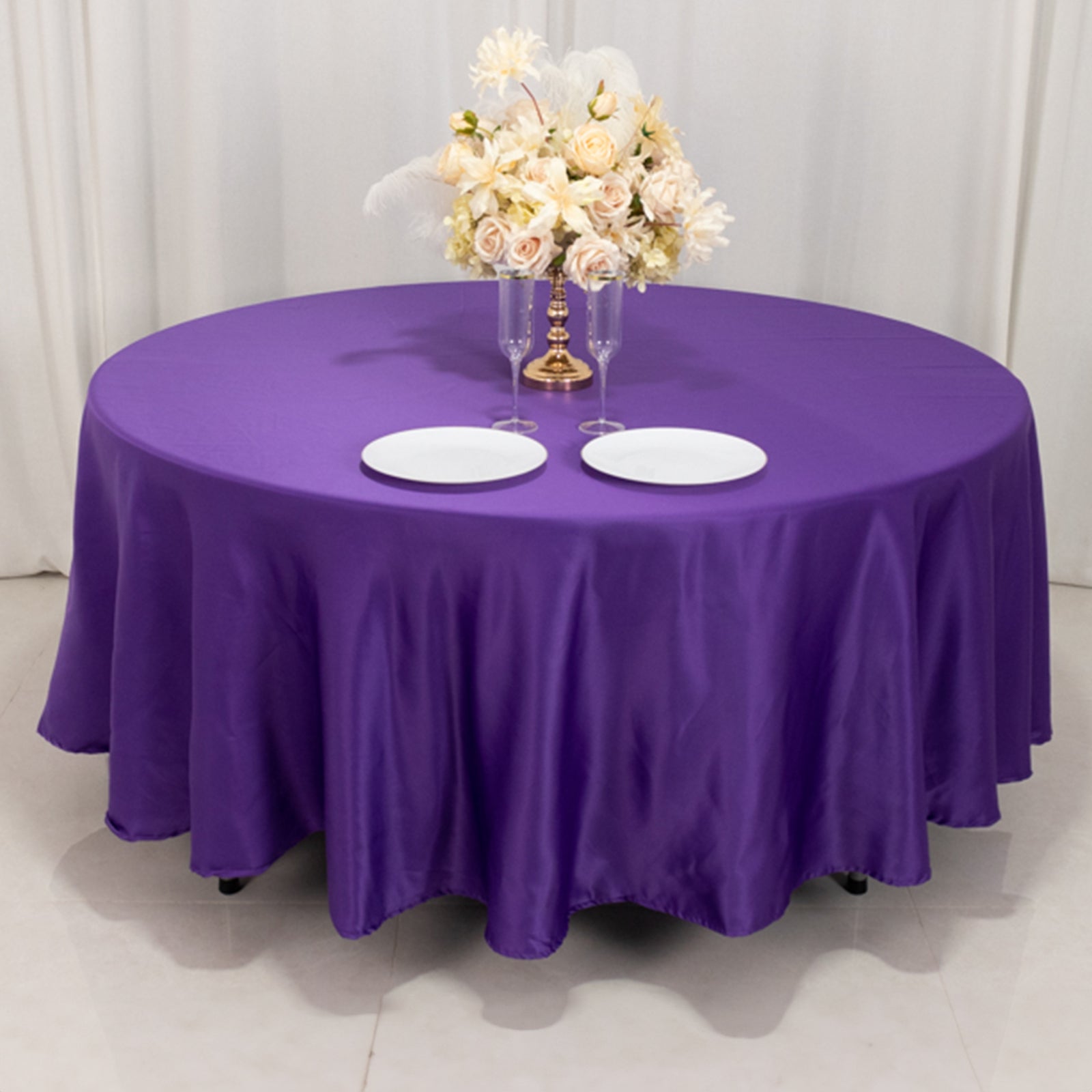 Purple satin round tablecloth on a table with floral arrangement.