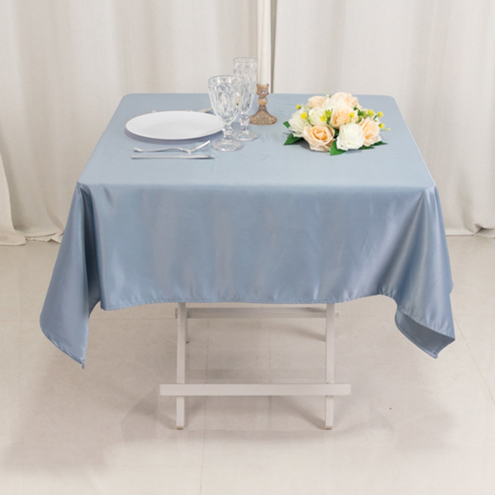 Dusty blue satin square tablecloth on a table with plates and flowers.