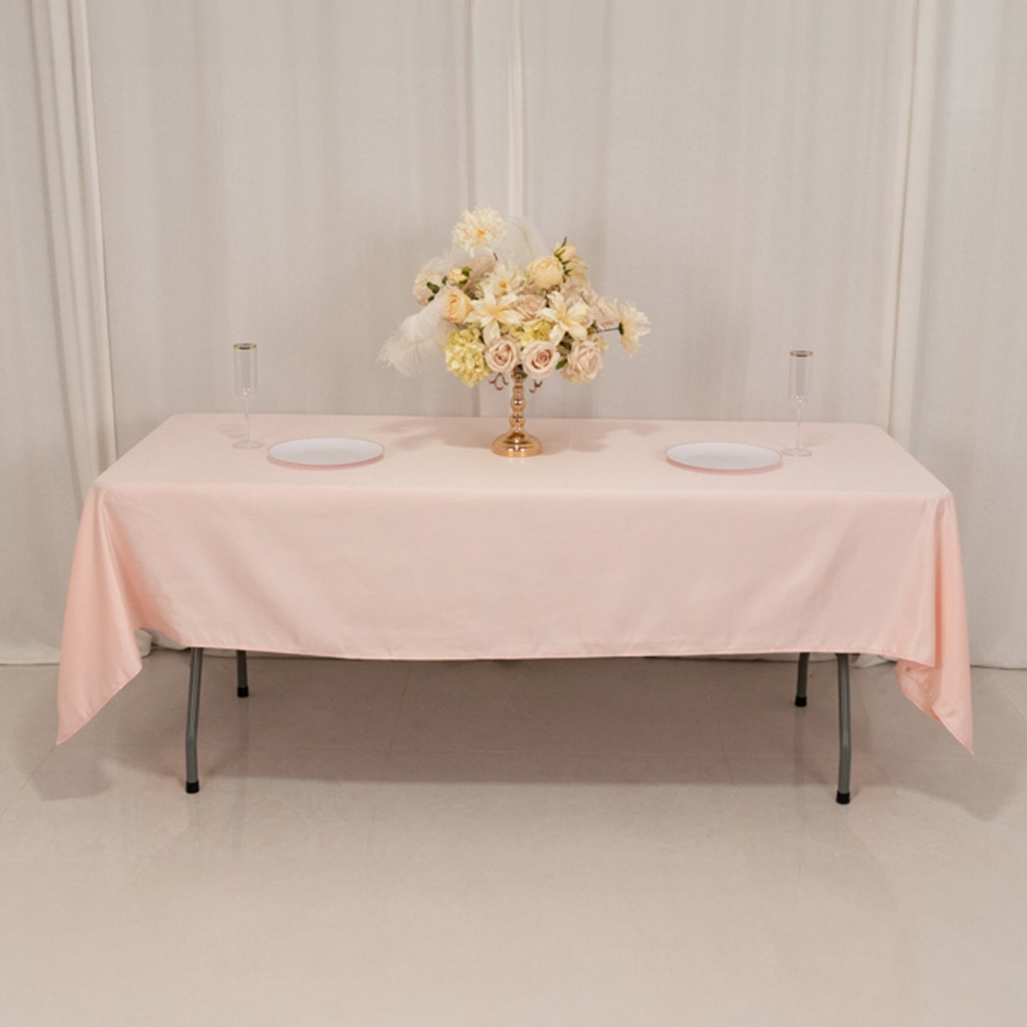 Blush satin tablecloth draped over a rectangle table with floral arrangement.