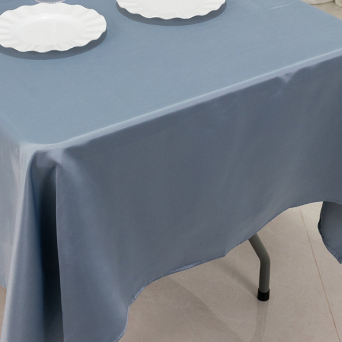 Dusty blue satin rectangle tablecloth on a table with white plates.
