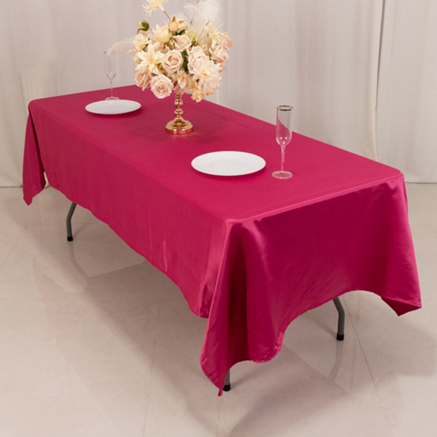 Fuchsia satin rectangle tablecloth on a table with floral centerpiece and glassware.
