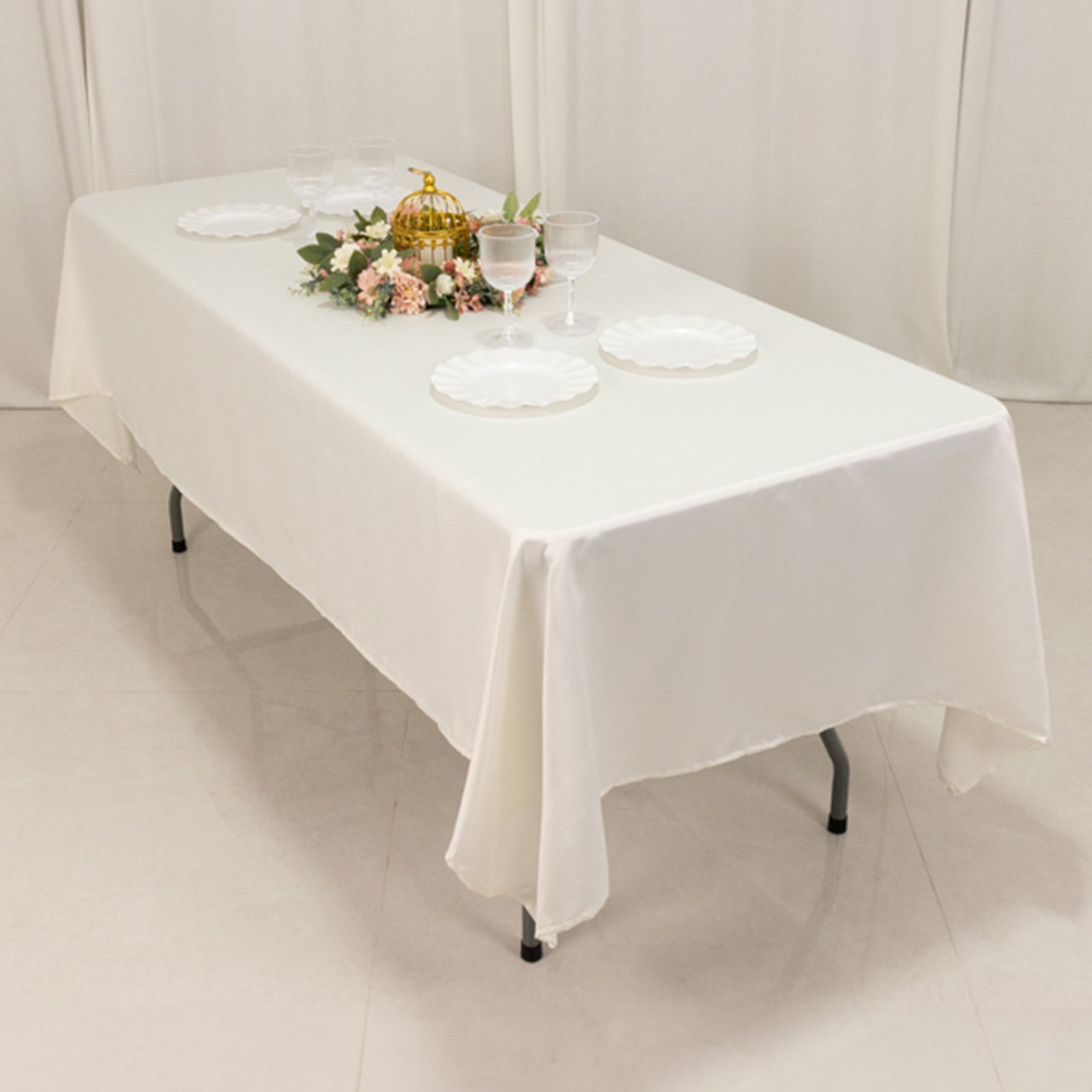 Ivory satin rectangle tablecloth on a dining table with decorative items.