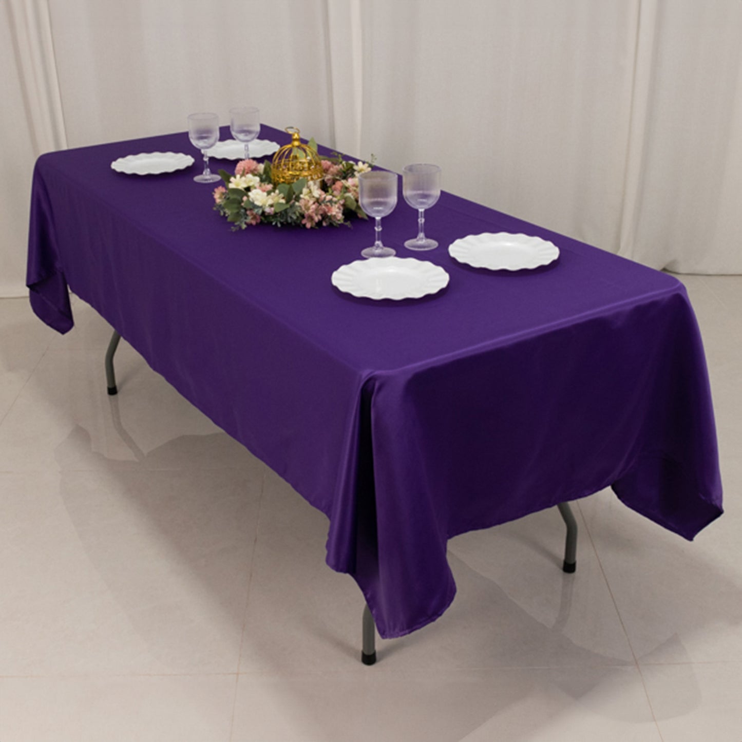 Purple satin rectangle tablecloth draped over a table with plates and glasses.