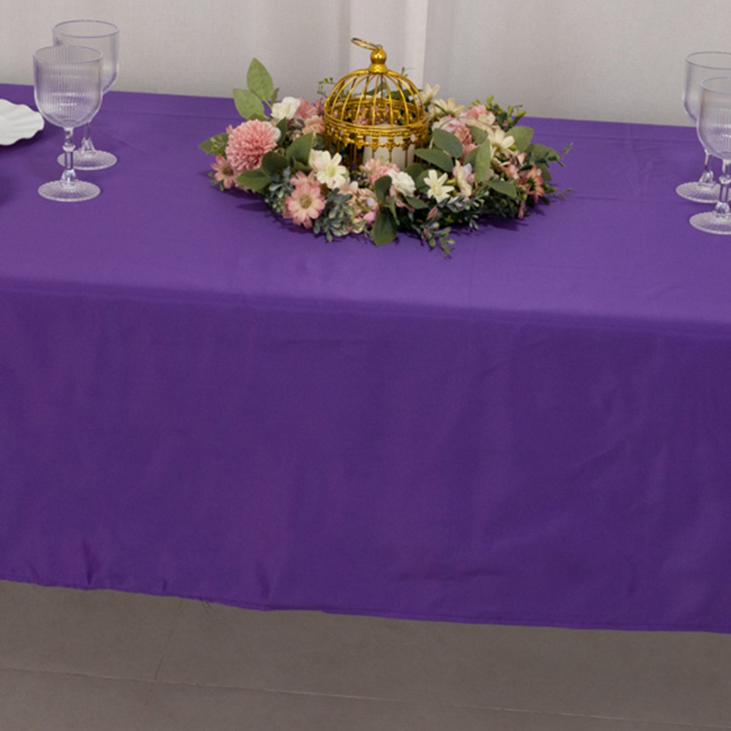 Purple rectangular tablecloth on a table with floral decor and glassware.