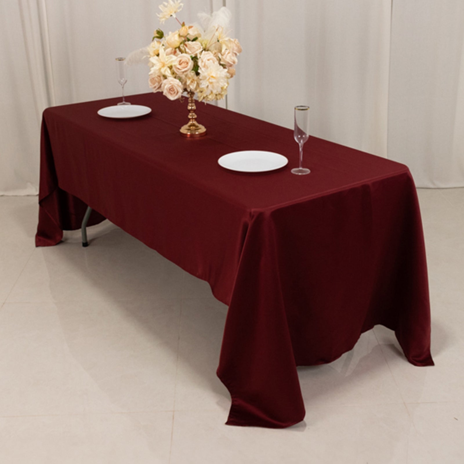Burgundy satin tablecloth on a table with floral centerpiece and dinnerware.