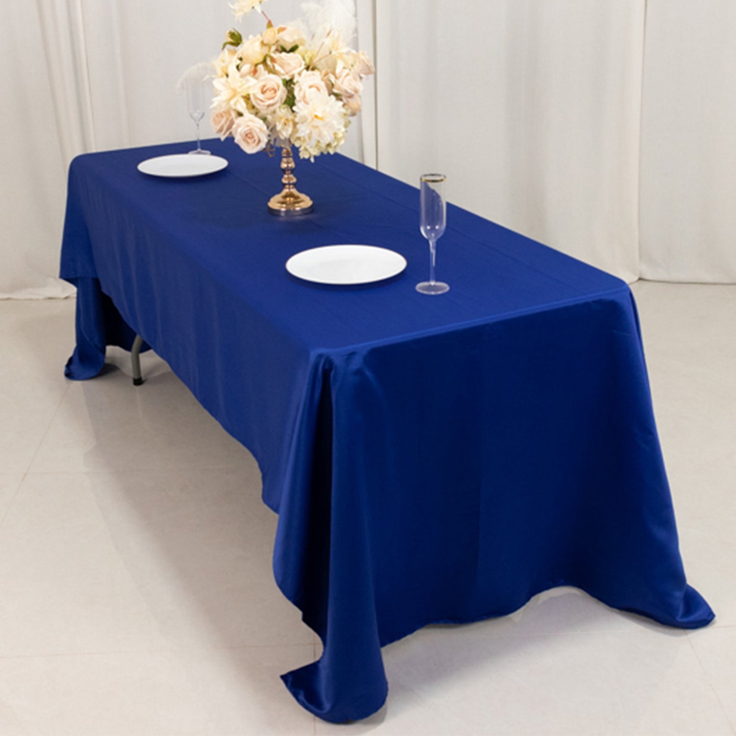 Royal blue satin rectangle tablecloth on a dining table with floral arrangement.