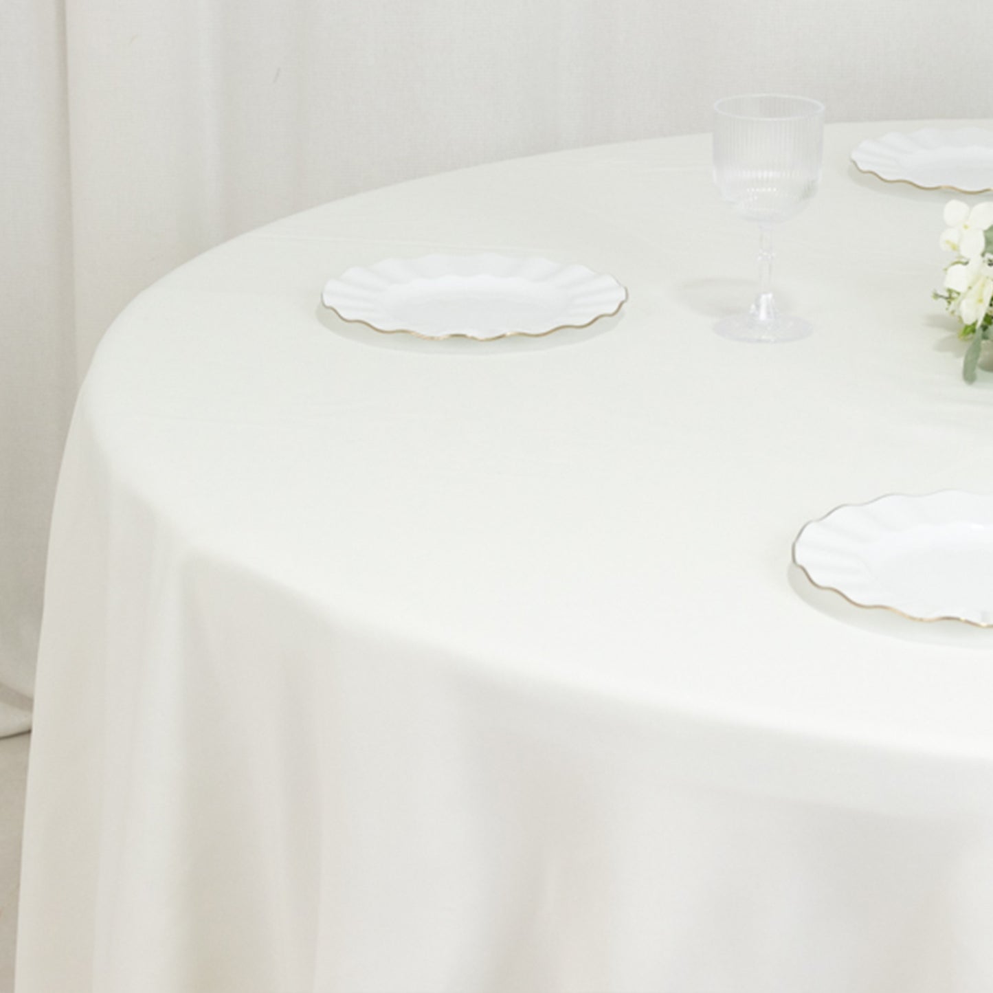 Ivory round tablecloth on a table with white plates and a glass.