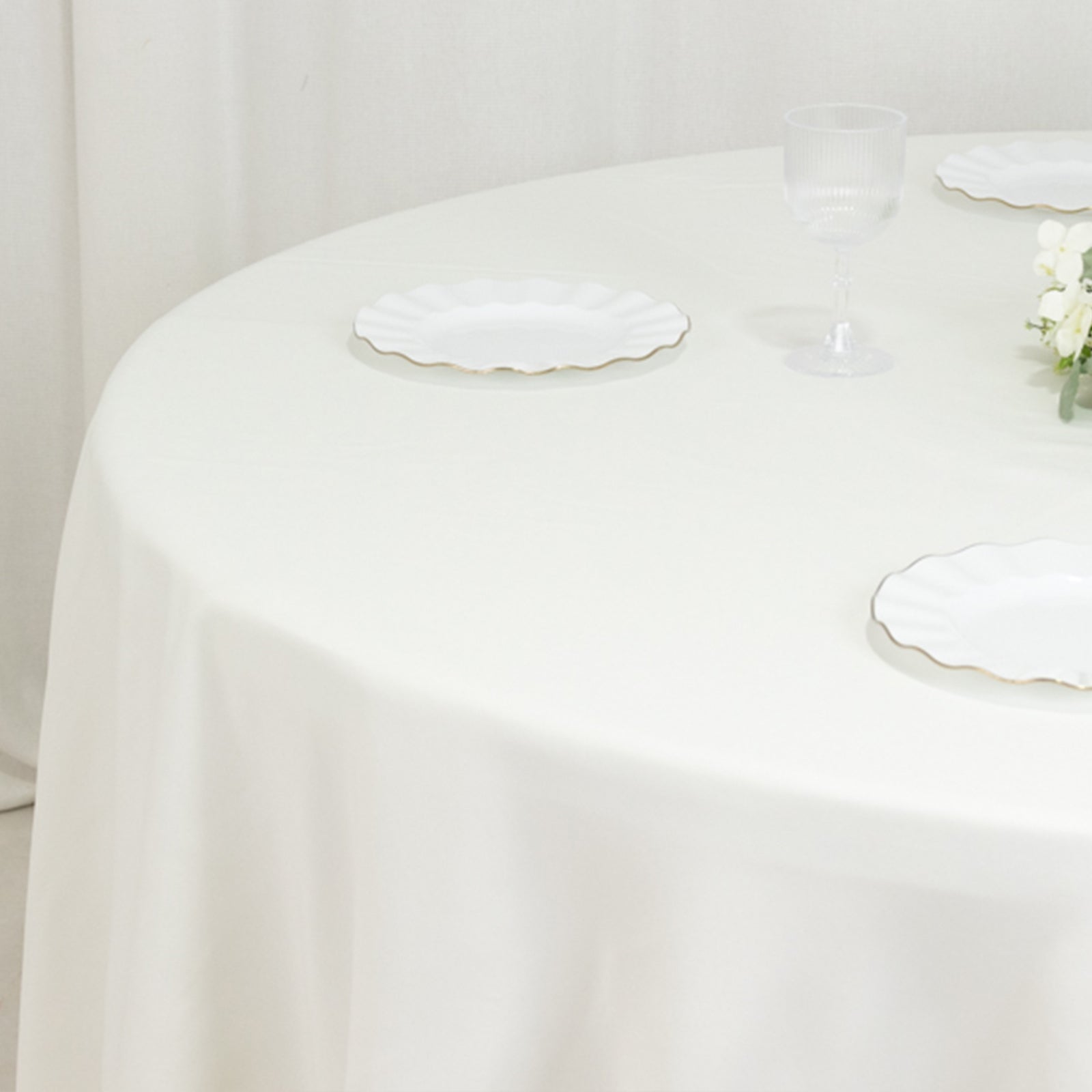 Ivory round tablecloth on a table with white plates and a glass.