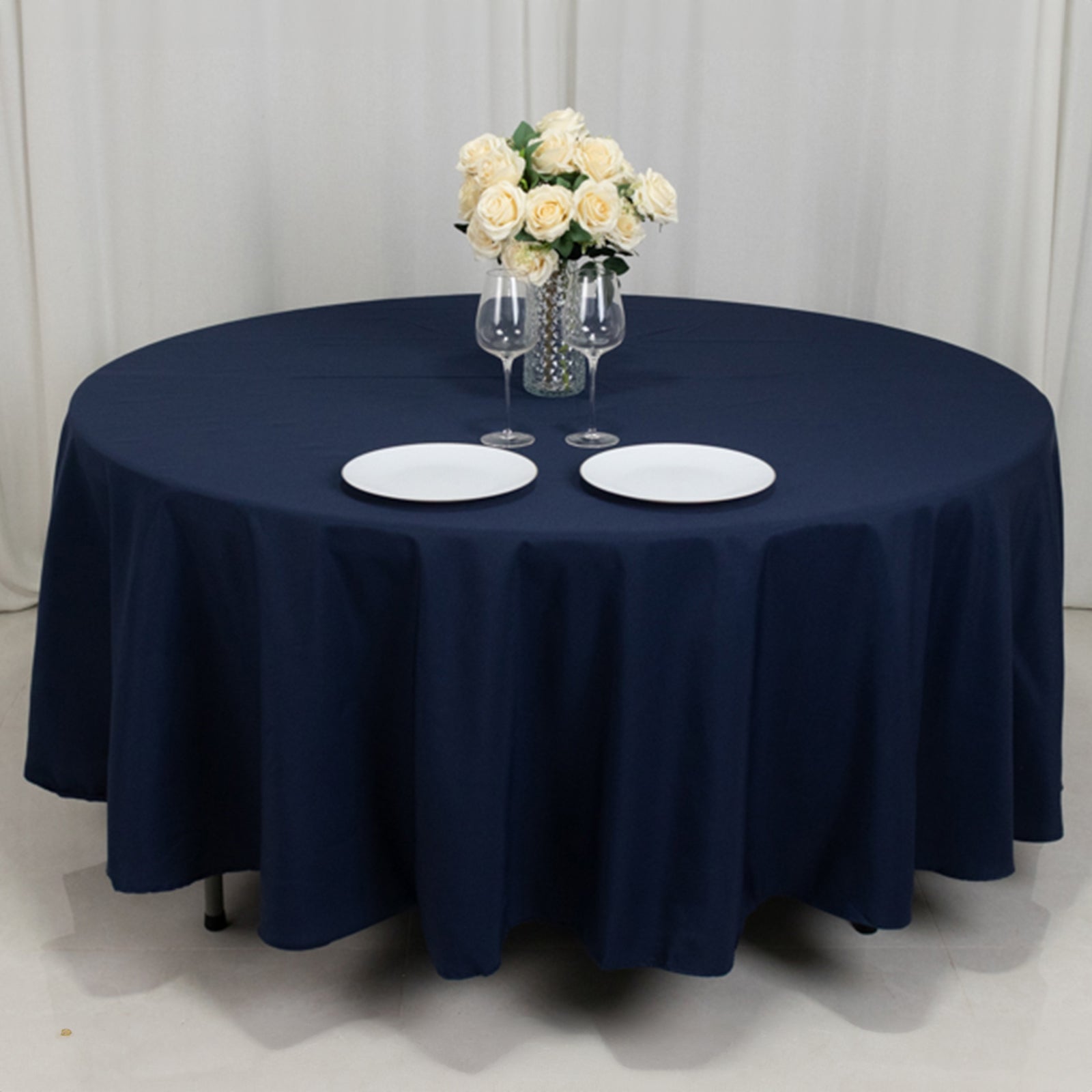 Navy blue round tablecloth on a table with plates and a floral centerpiece.