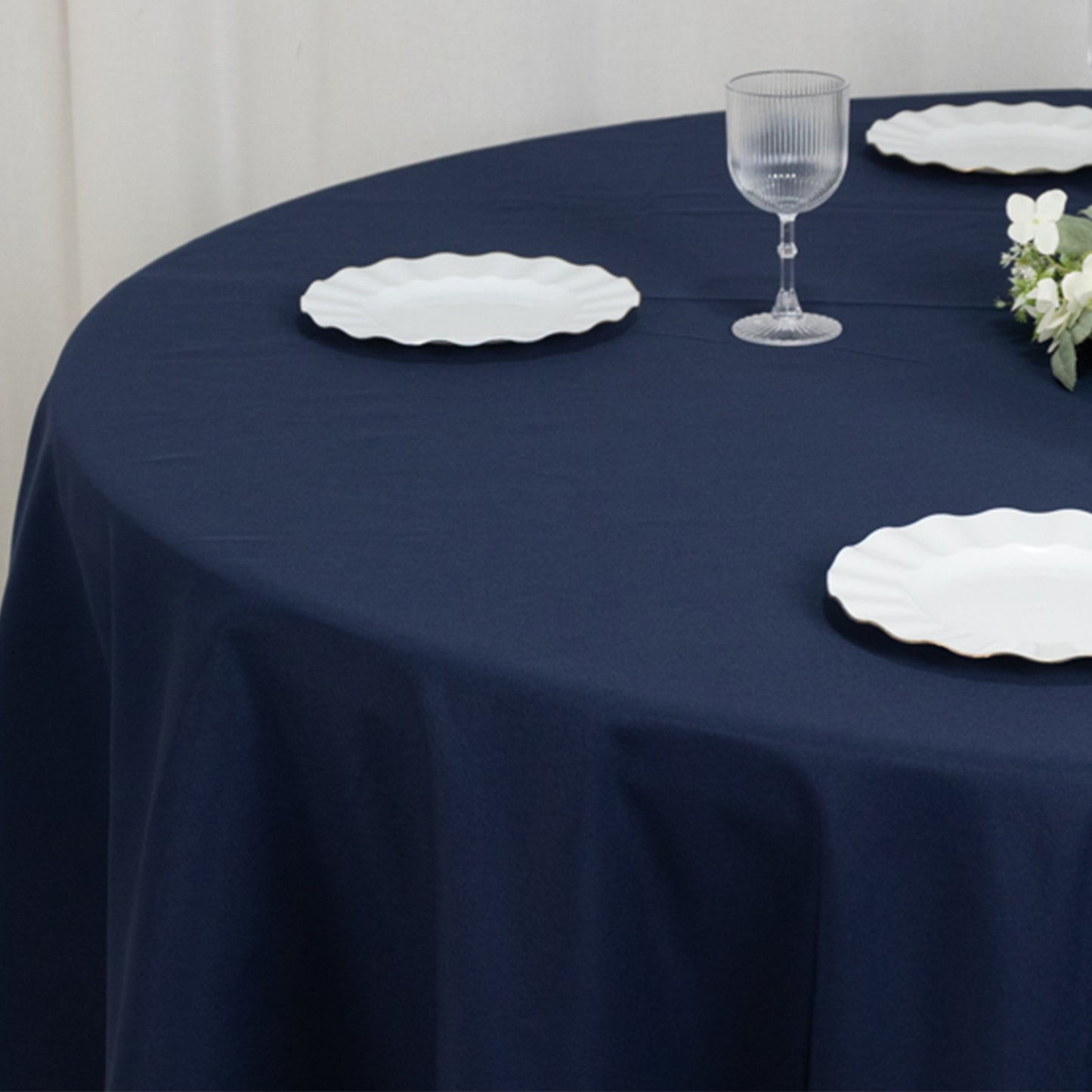 Navy blue round tablecloth on a dining table with white plates and glass.