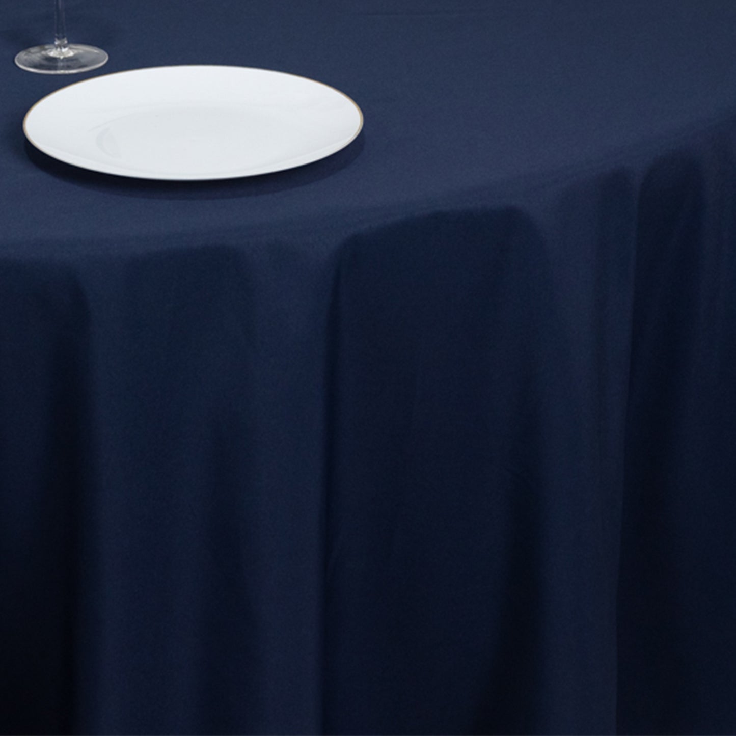 Navy blue round tablecloth on a table with a plate and glass.