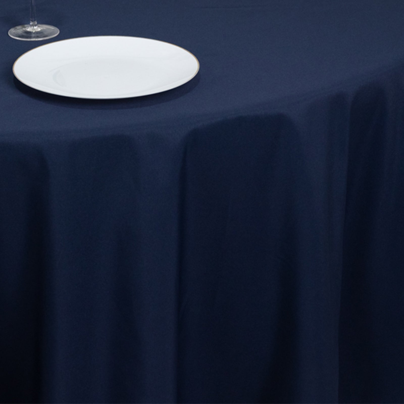 Navy blue round tablecloth on a table with a plate and glass.