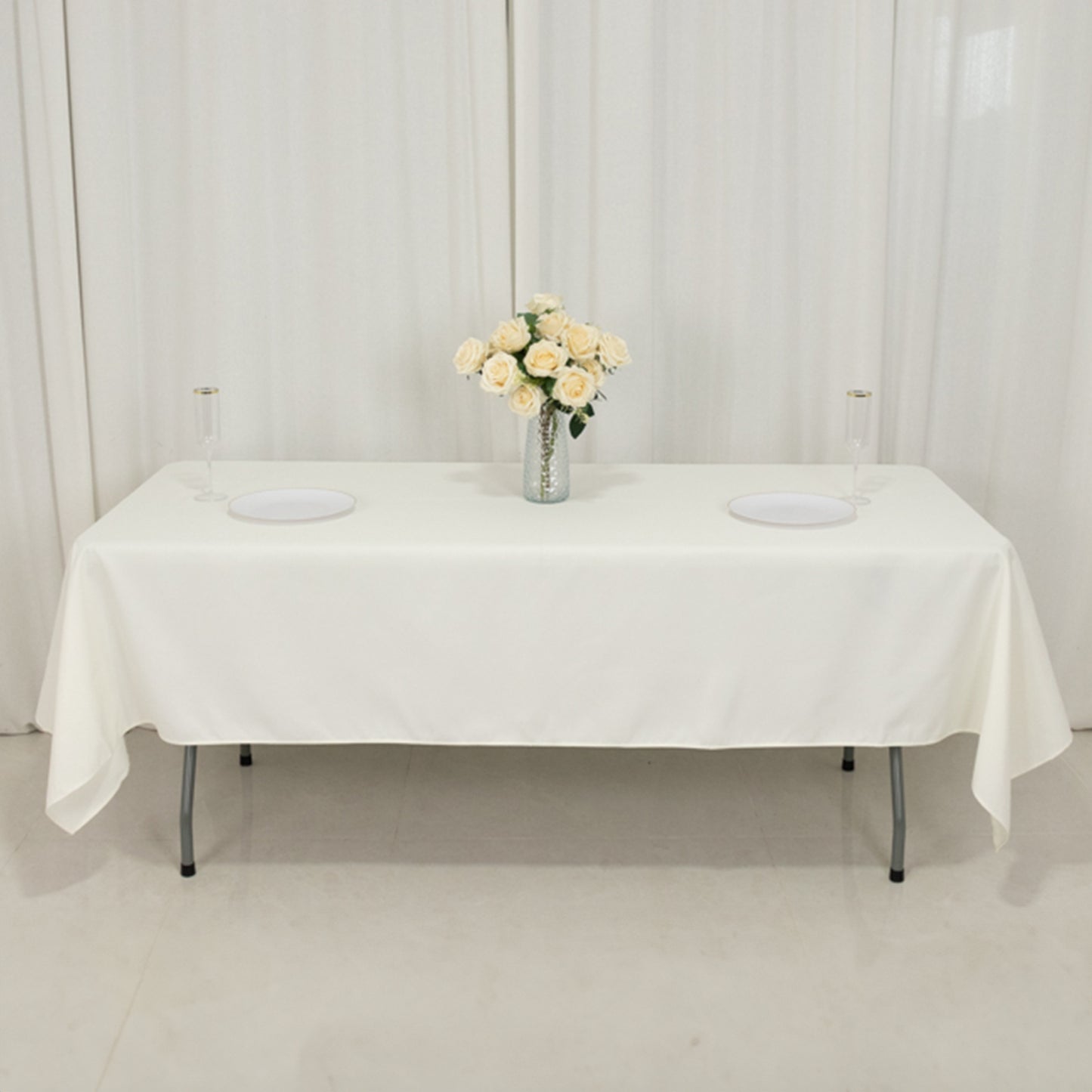Ivory fire retardant rectangular tablecloth on a table with flowers and plates.