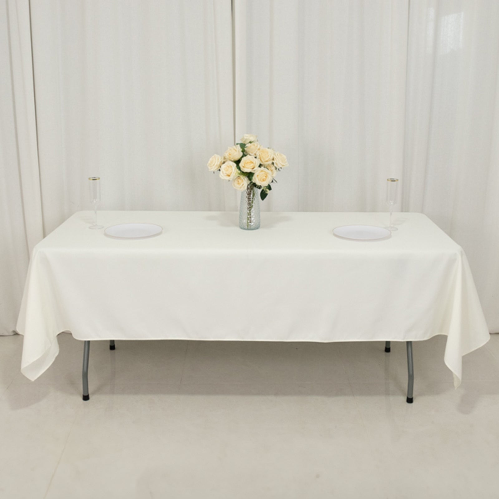 Ivory fire retardant rectangular tablecloth on a table with flowers and plates.