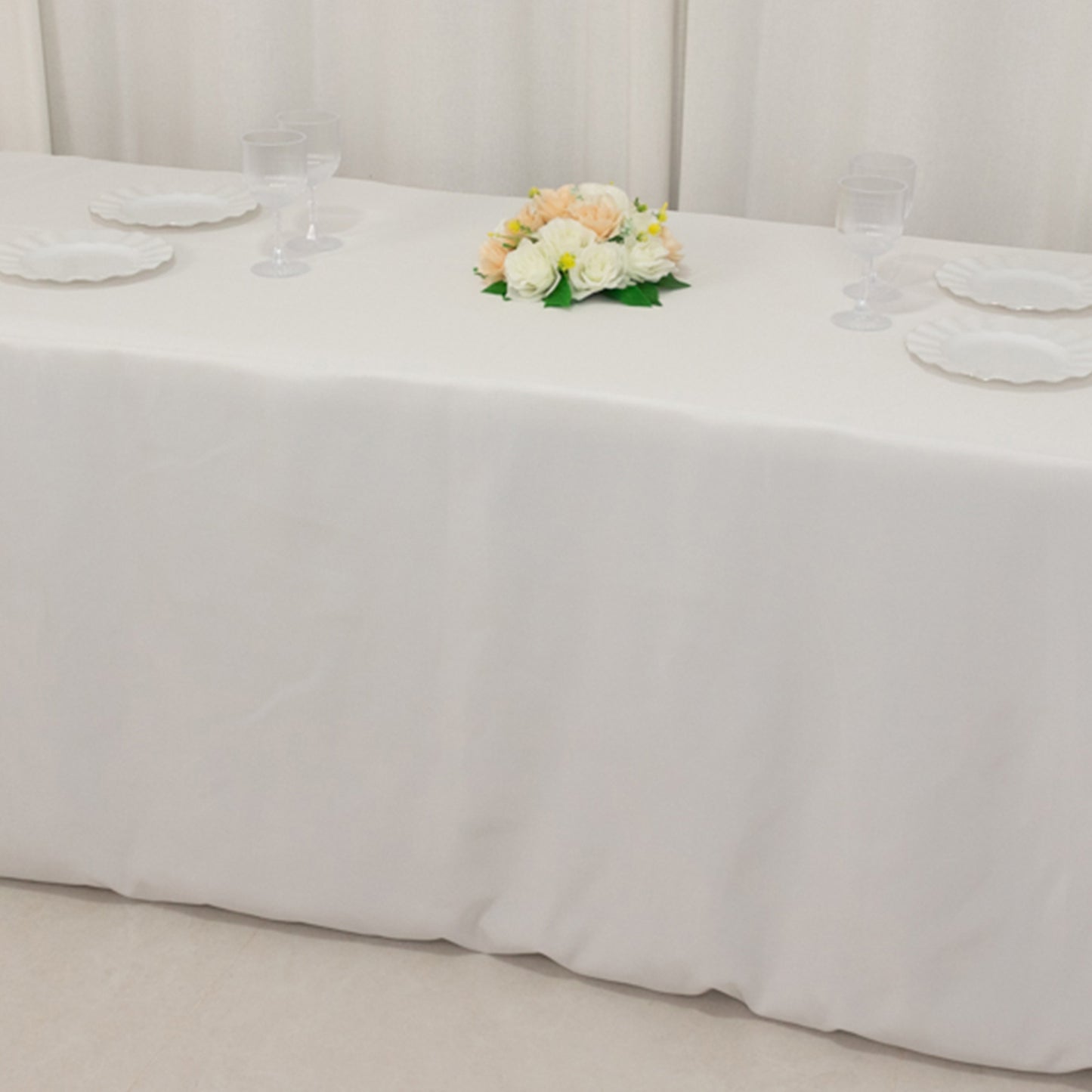 White fitted tablecloth on a rectangular table with floral decor.