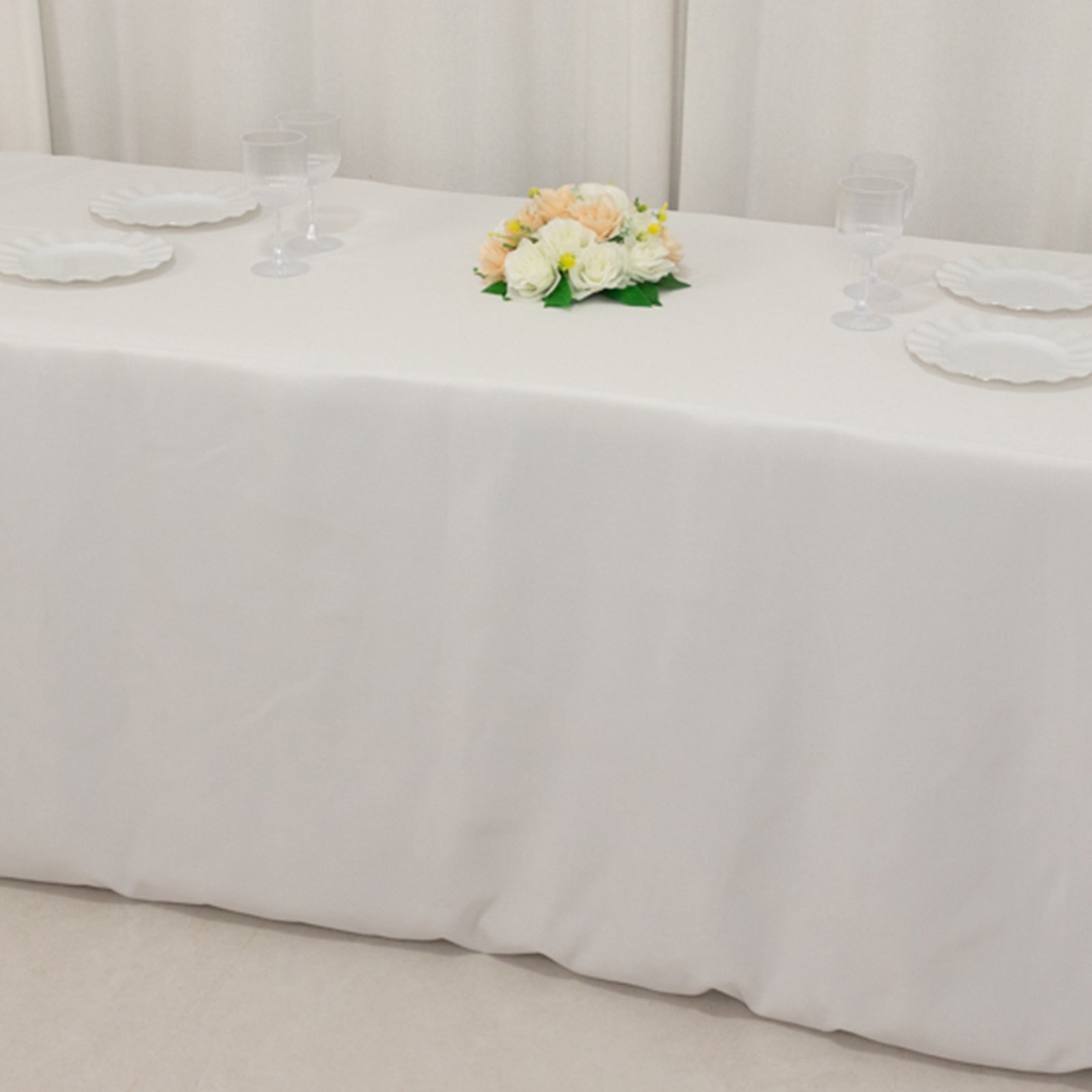 White fitted tablecloth on a rectangular table with floral decor.