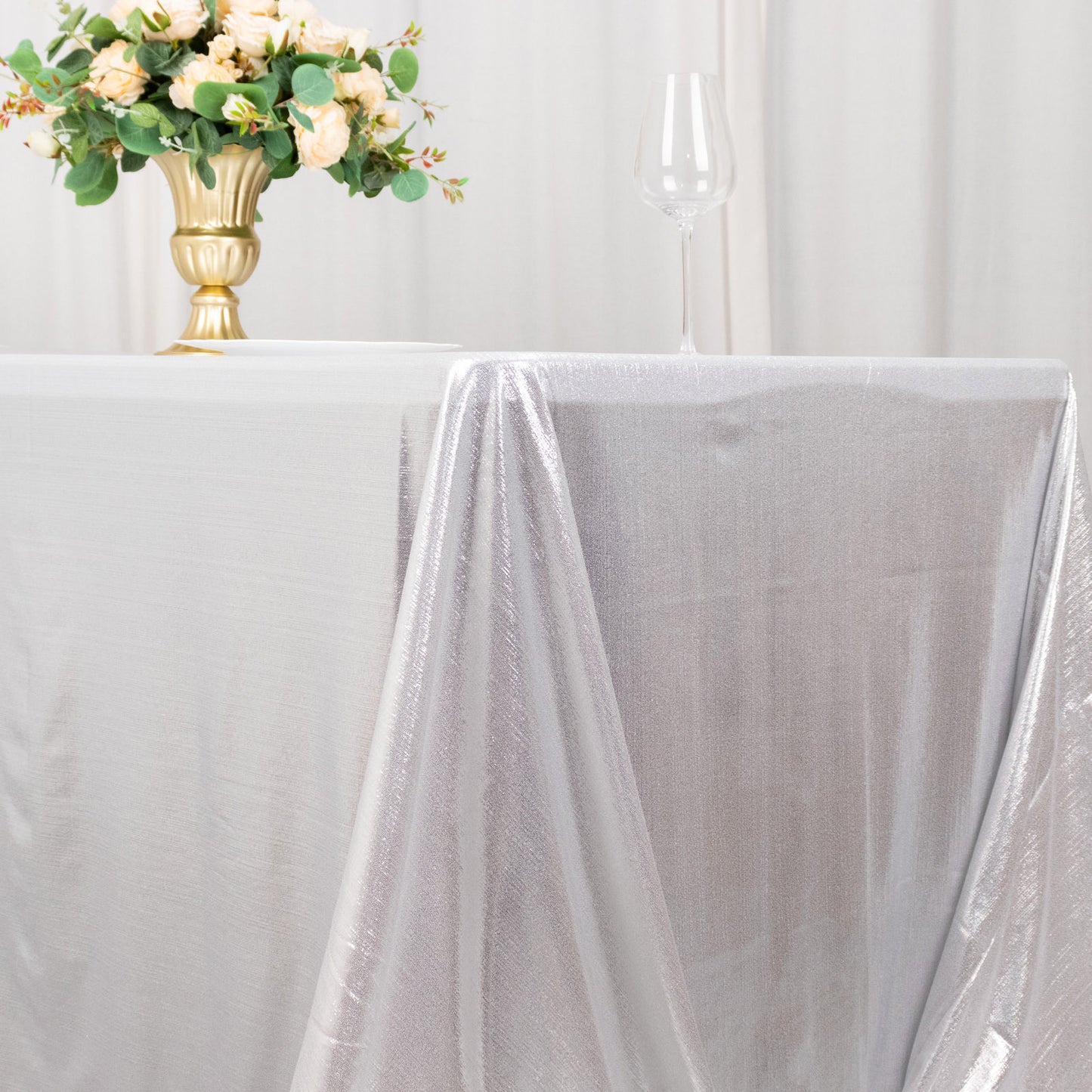 Silver shimmer sequin dot tablecloth on a table with flowers and glassware.