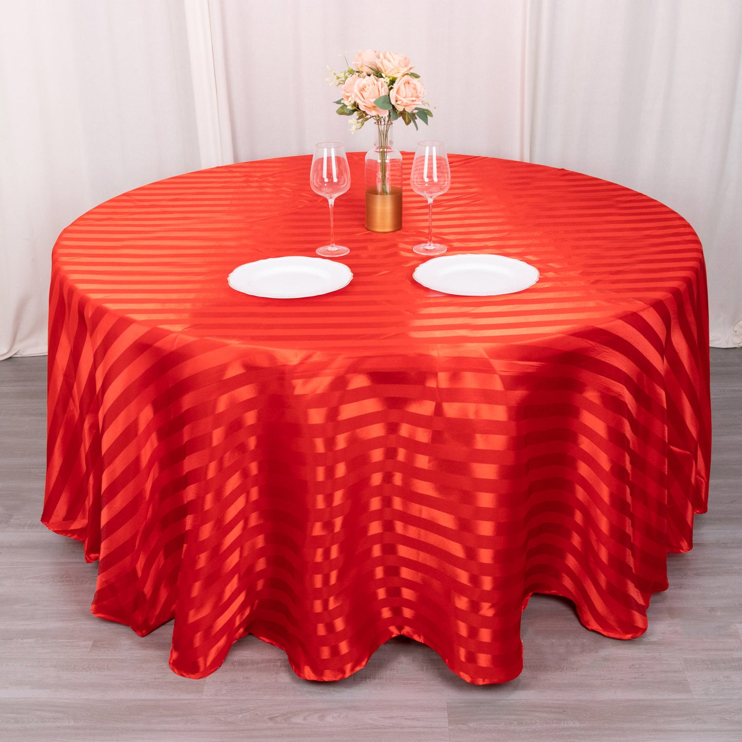 120" red satin stripe seamless round tablecloth on a table with flowers and dinnerware.
