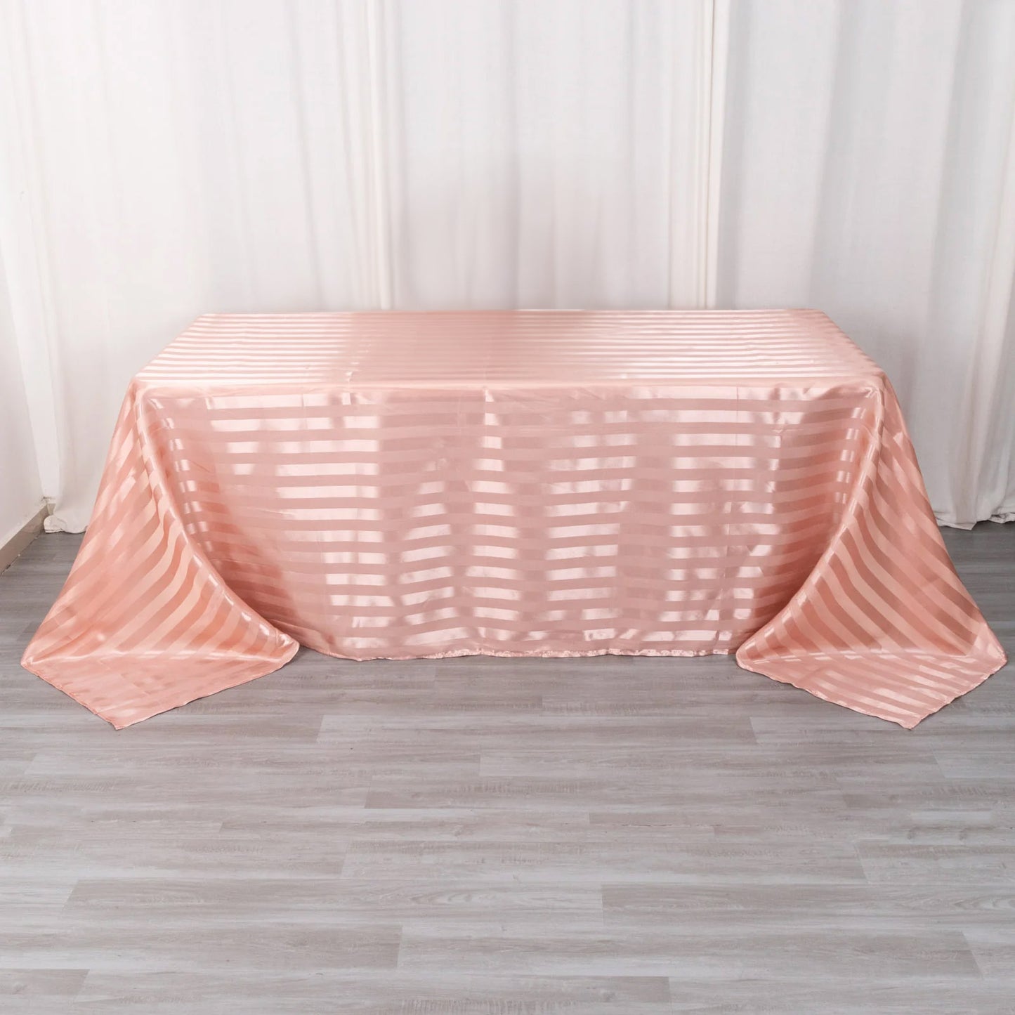 Dusty rose satin stripe rectangular tablecloth on a wooden floor.