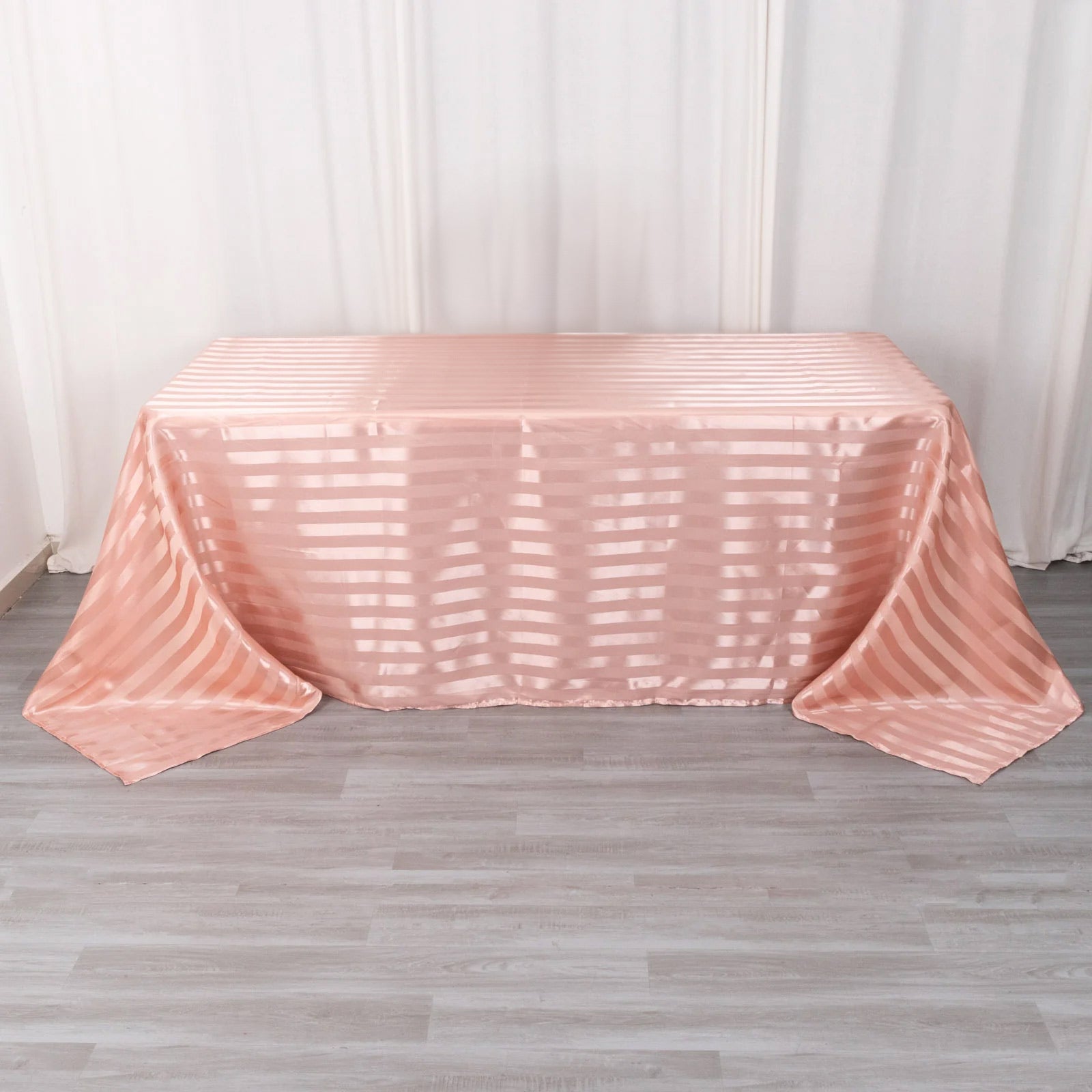 Dusty rose satin stripe rectangular tablecloth on a wooden floor.