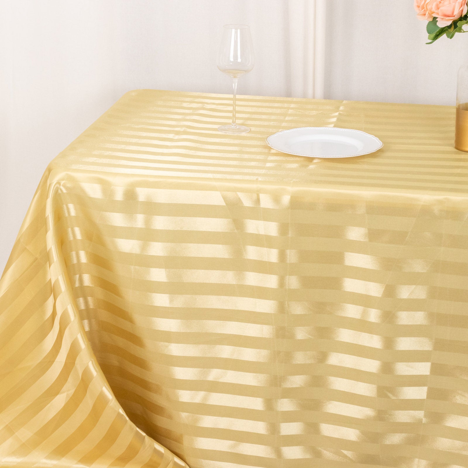 Champagne satin stripe rectangular tablecloth on a table with a glass and plate.