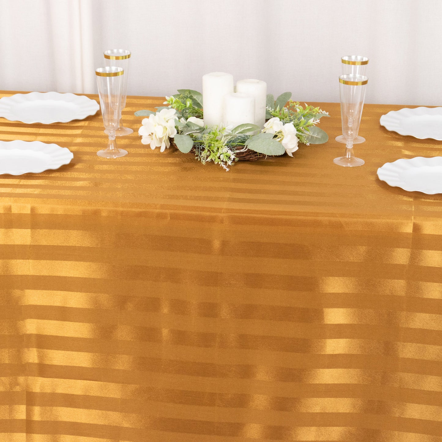 Gold satin stripe tablecloth on a dining table with decorative centerpieces.