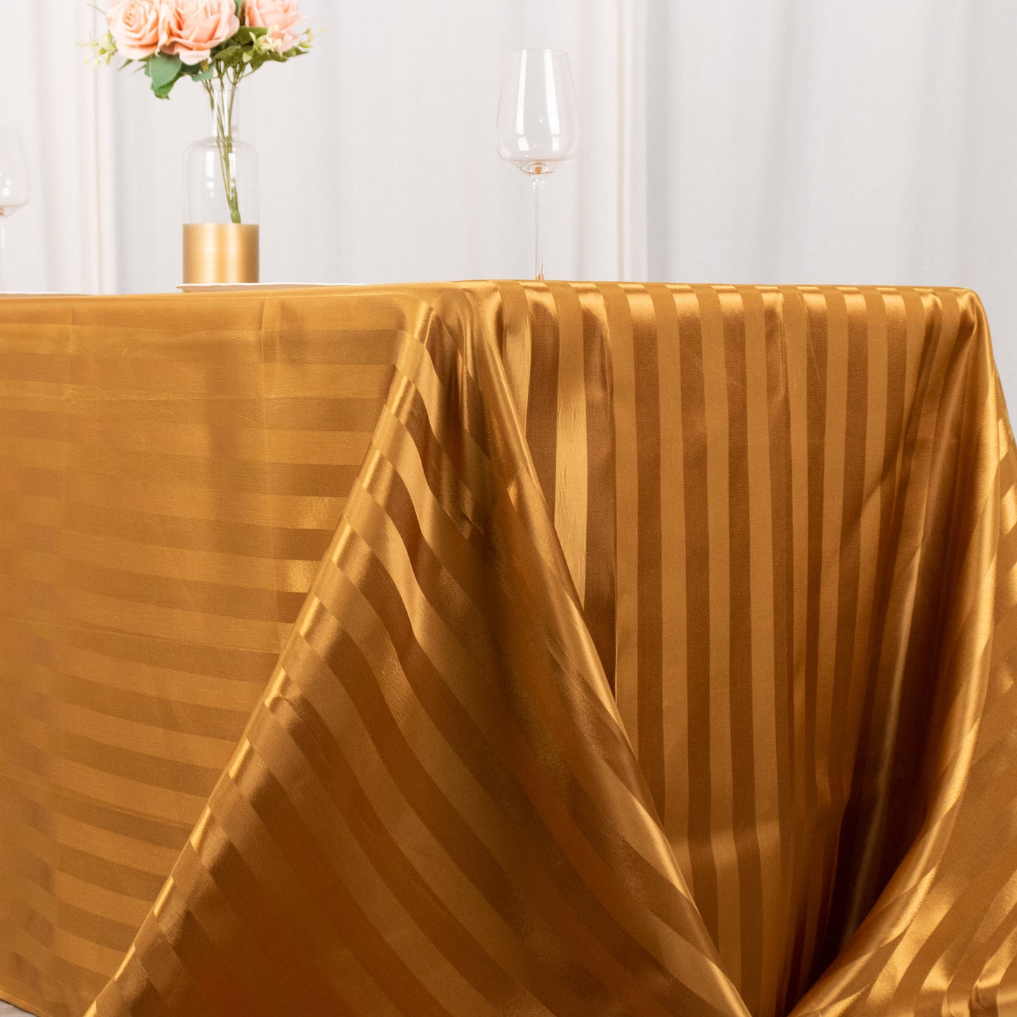Gold satin stripe tablecloth on a table with flowers and glassware.
