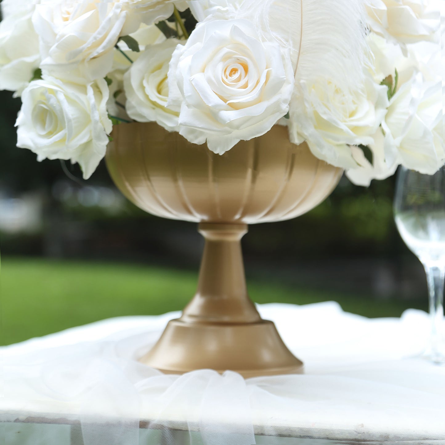 Gold metal compote vase filled with white roses, perfect for wedding centerpieces.