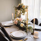 Gold metal wedding cake display stand with floral centerpiece on a dining table.