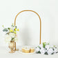 Gold metal arch wedding cake display stand with floral centerpiece and cupcakes.