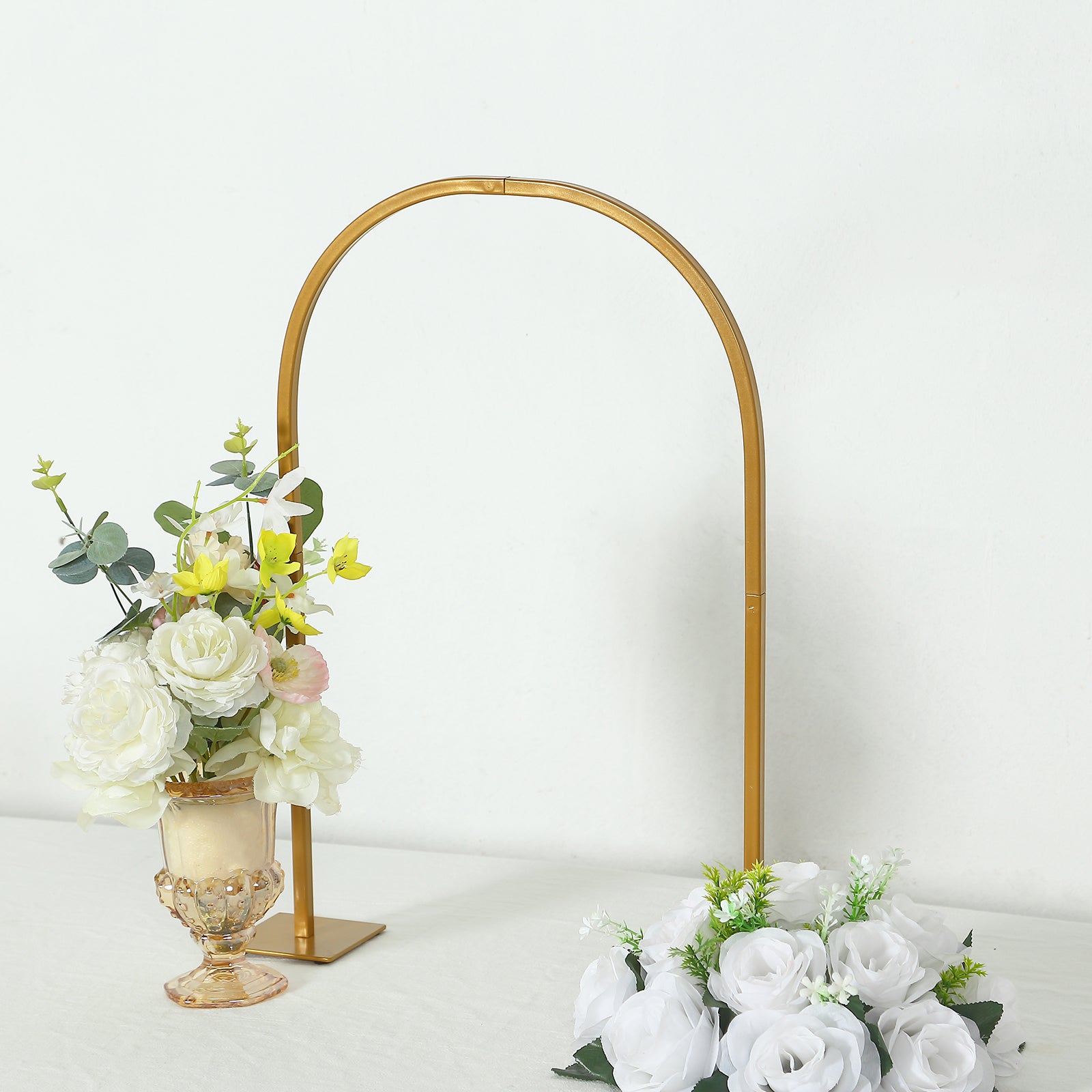 Gold metal chiara arch wedding cake display stand with floral centerpiece.