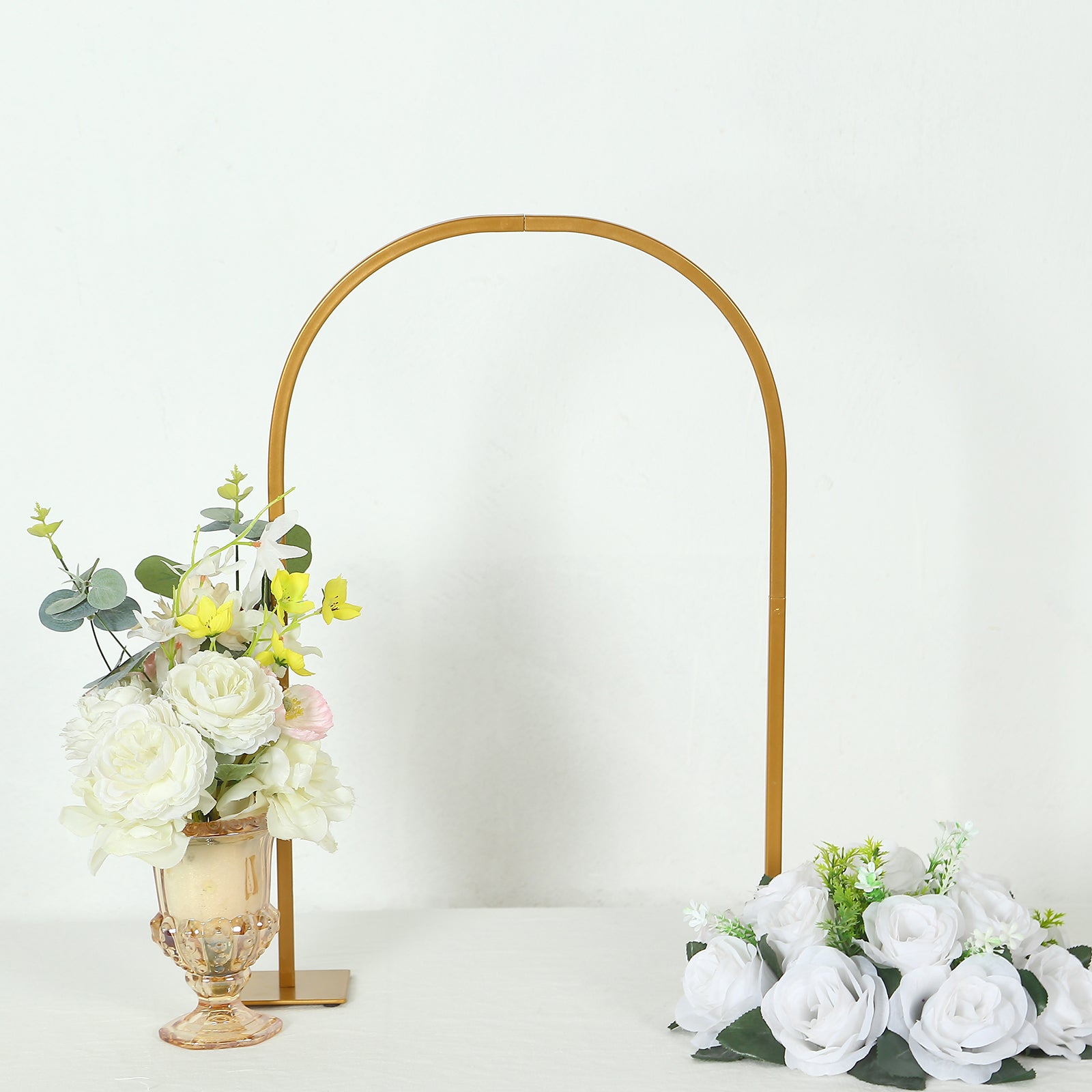 Gold metal Chiara arch wedding cake display stand with flowers.
