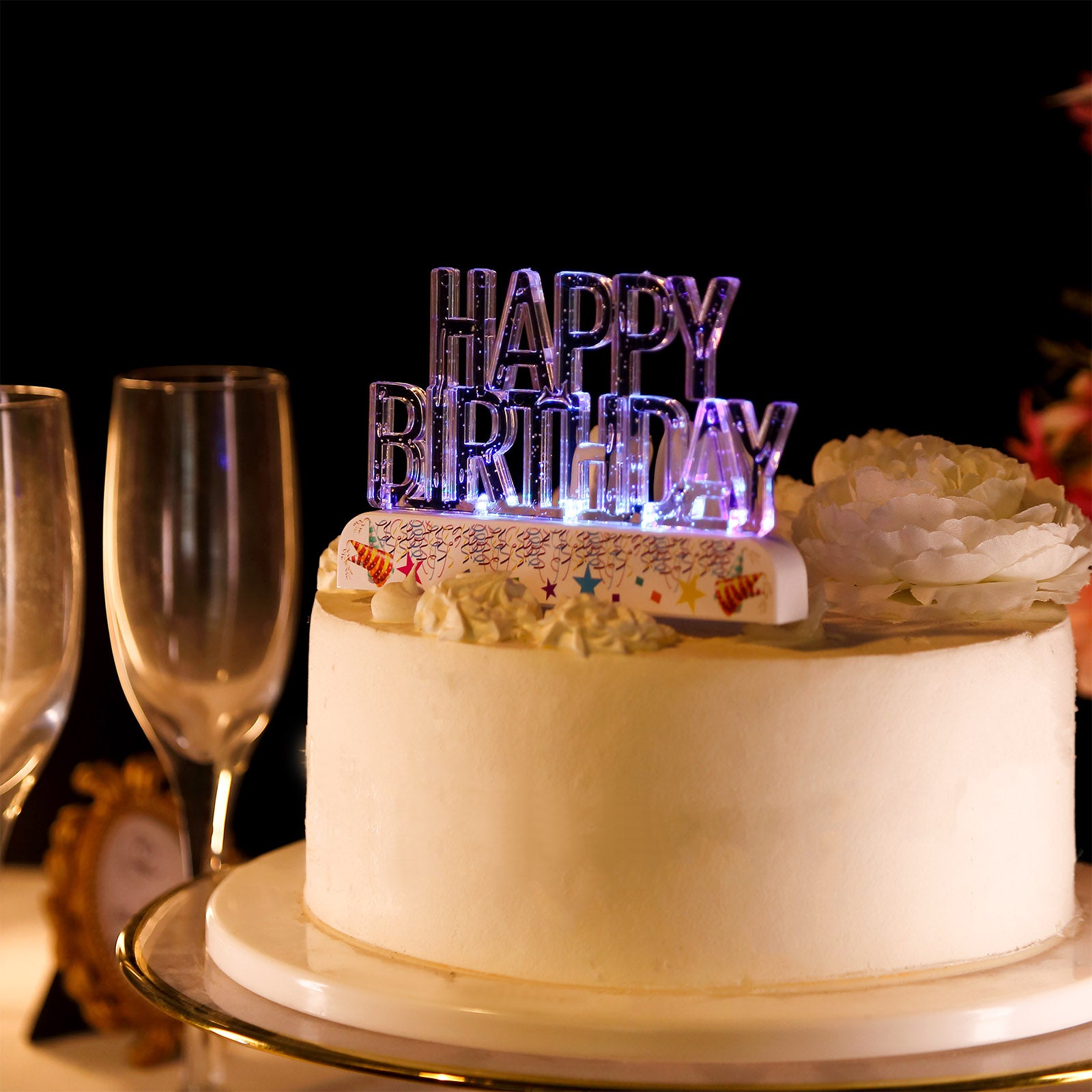 Clear acrylic multicolor flashing LED birthday cake topper on a white cake.