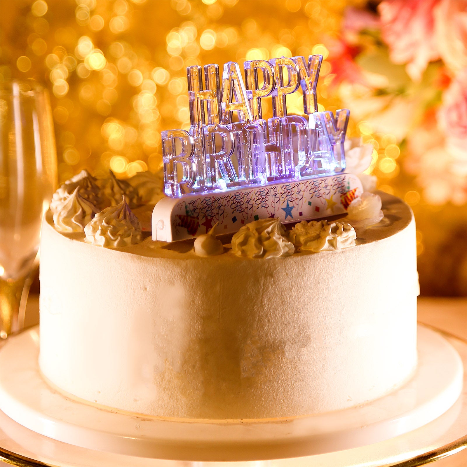 Clear acrylic multicolor flashing LED birthday cake topper on a white cake.