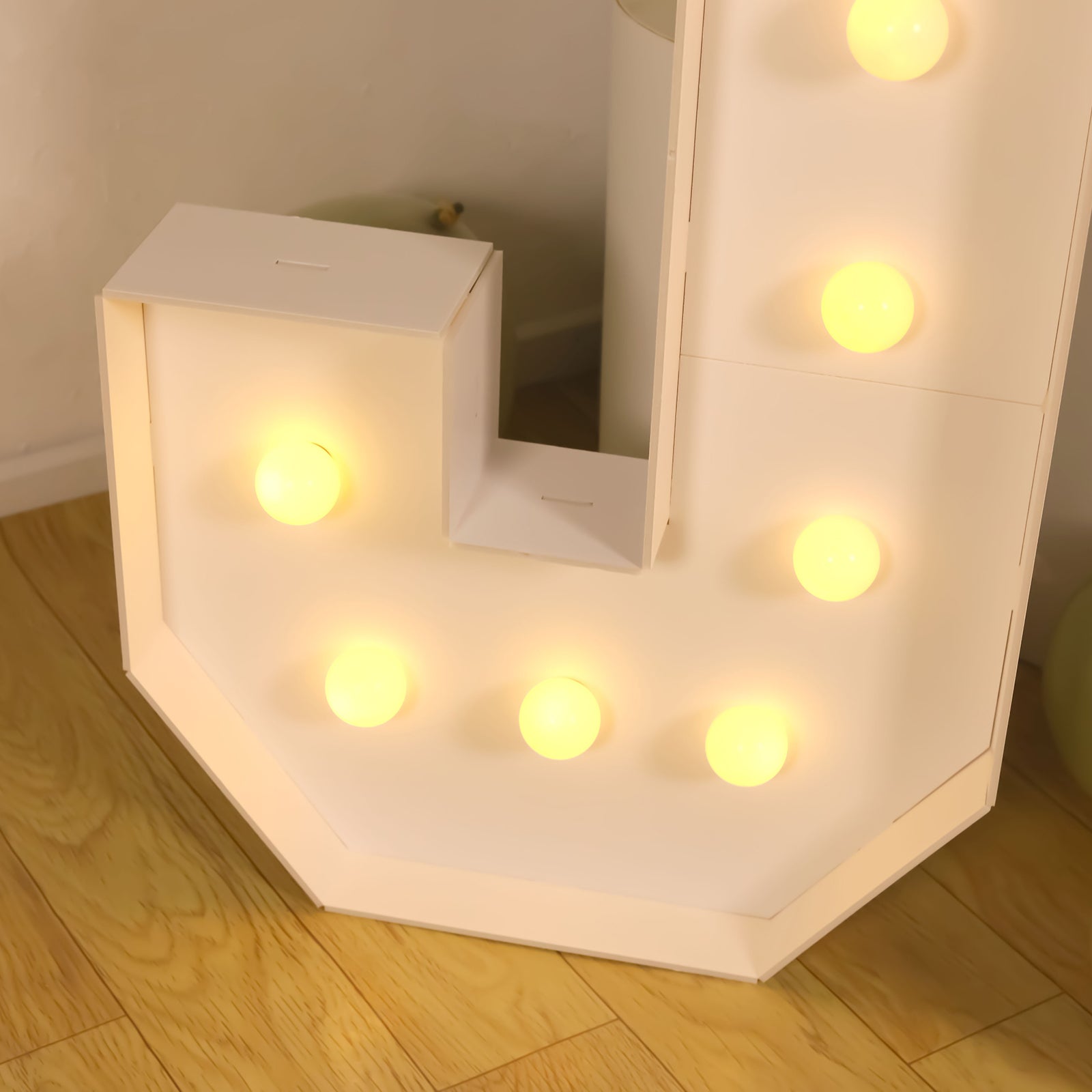 White LED marquee letter "J" with warm white lights on a wooden floor.