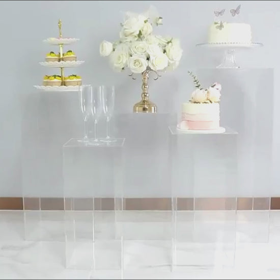 Clear acrylic pedestal stands displaying desserts and flowers.